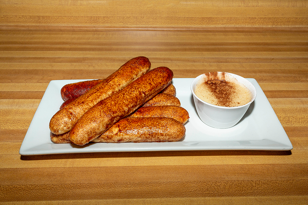 Plate of cinnamon sugar churros with a small cup of dipping sauce on a wooden table