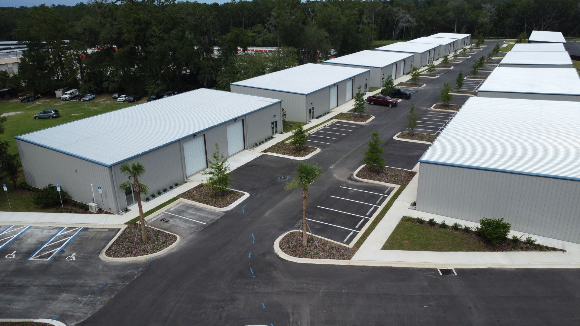 Aerial view of a commercial warehouse complex with white-roofed buildings and parking lots lined by trees