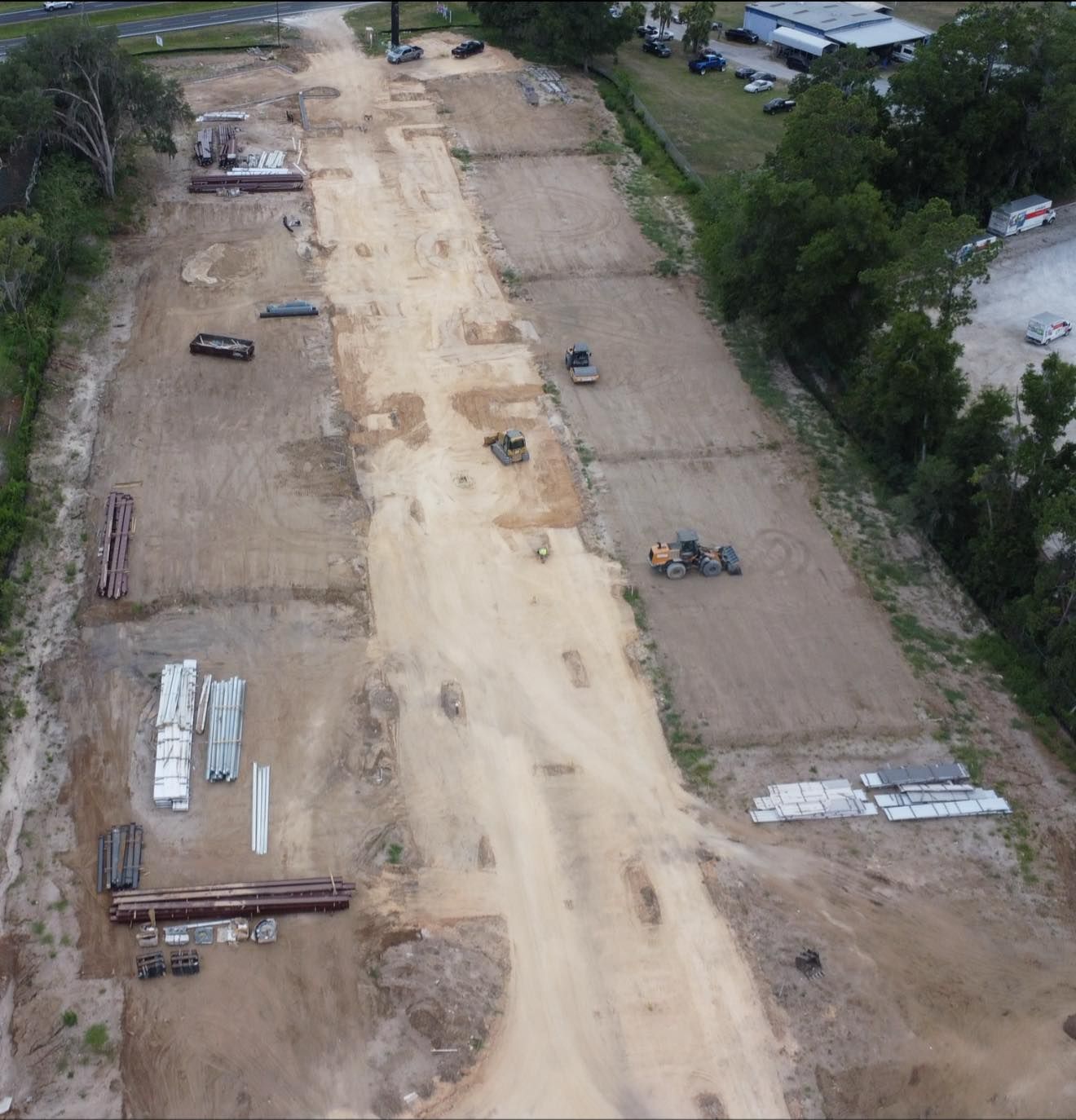 Aerial view of a construction site with a long cleared dirt path and scattered equipment.