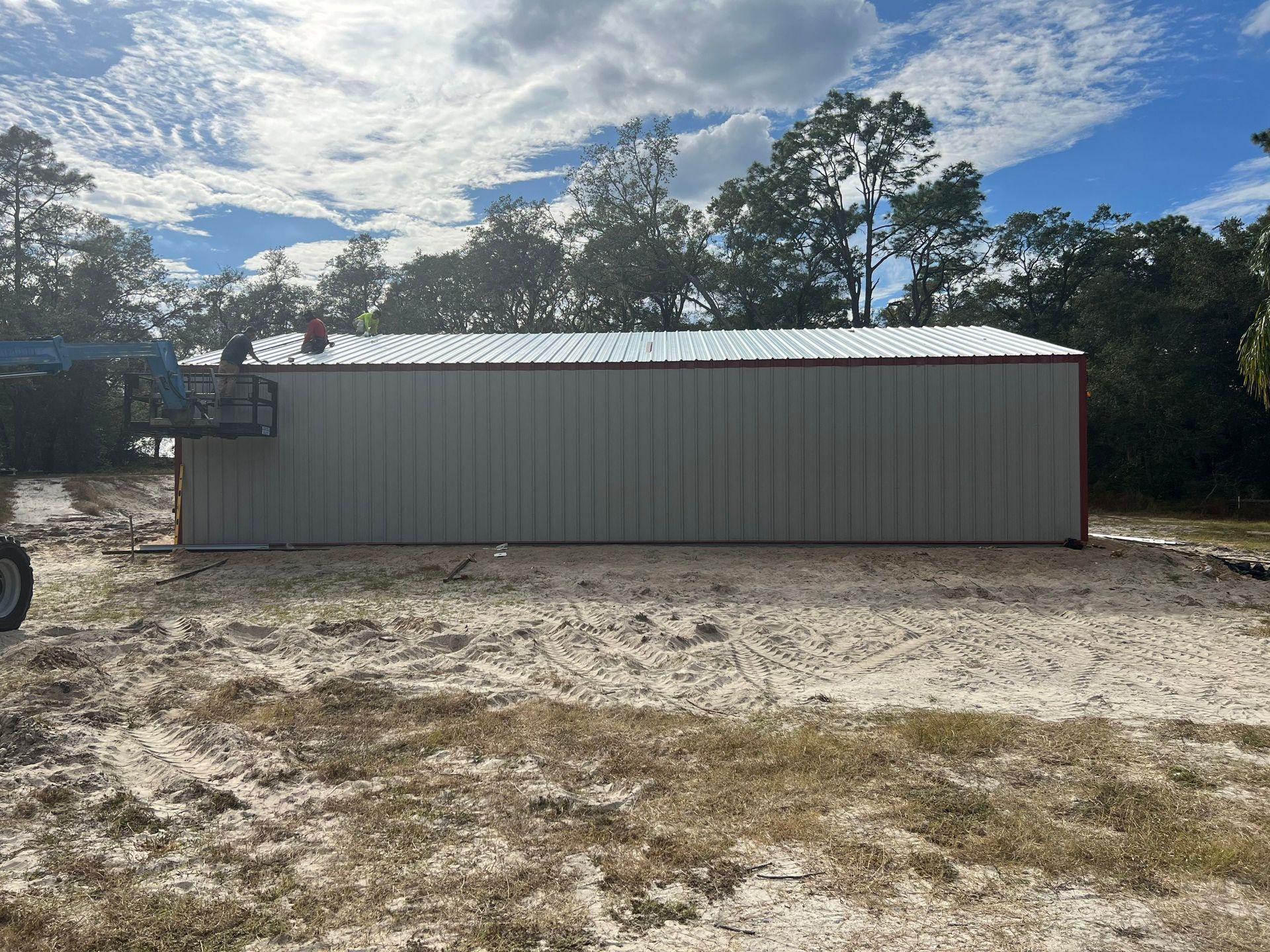 Small gray metal shed with a white roof on a dirt lot under a cloudy blue sky.
