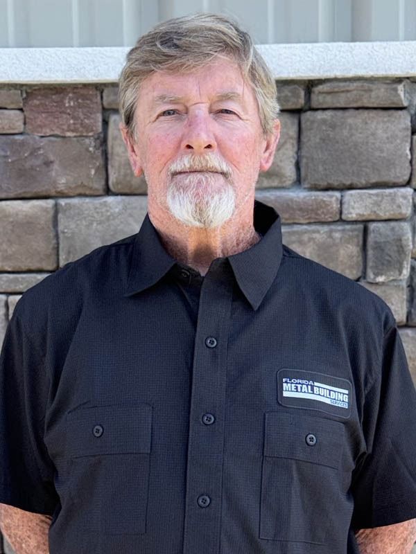 A person wearing a black uniform shirt with a logo stands against a stone wall background.