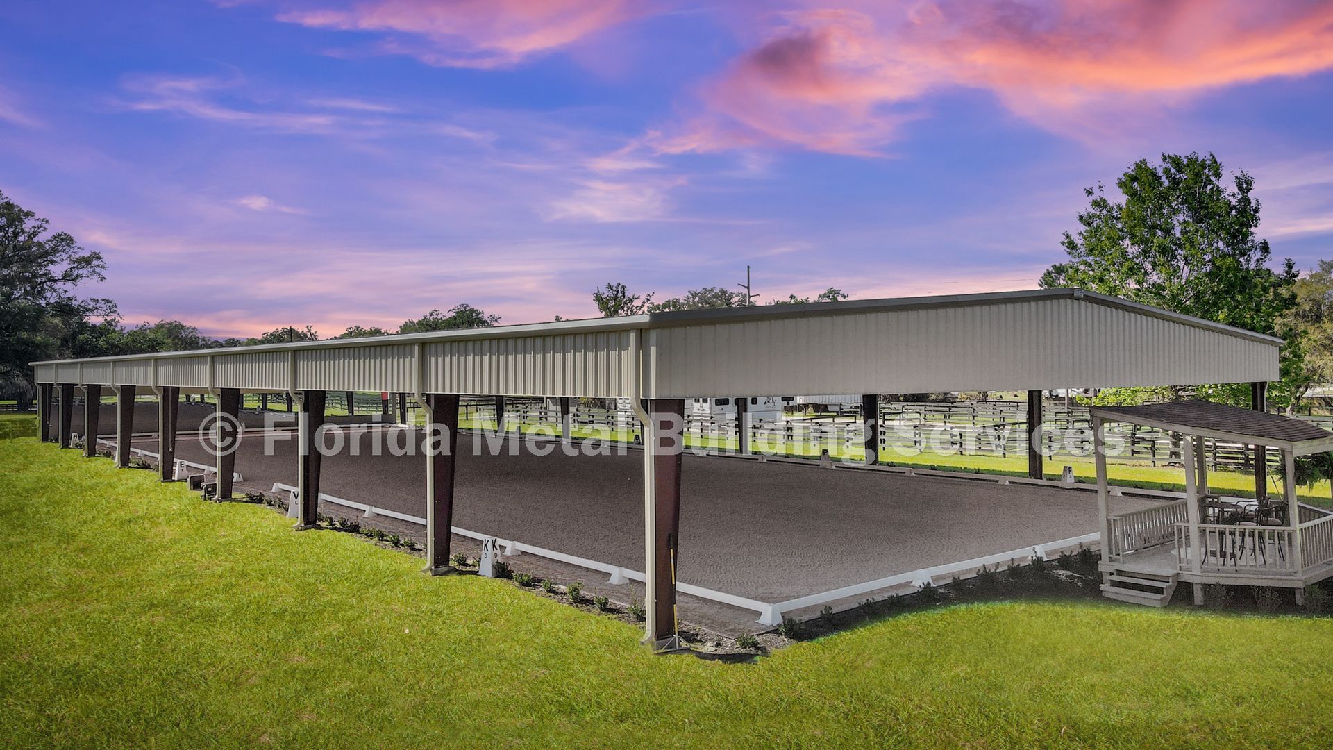 Open-sided livestock shelter in a grassy field at sunset, with purple clouds and distant trees.
