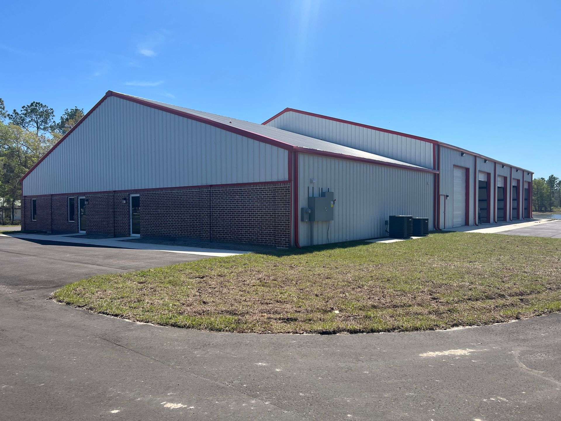 Large metal warehouse building with red trim, partial open side, and grassy lot under a clear blue sky