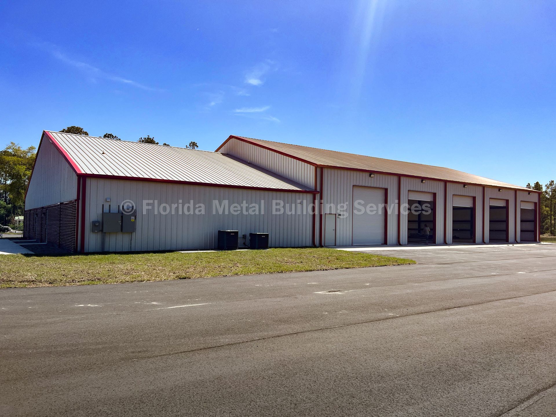 Red metal auto repair building with garage bays along a quiet road under a blue sky