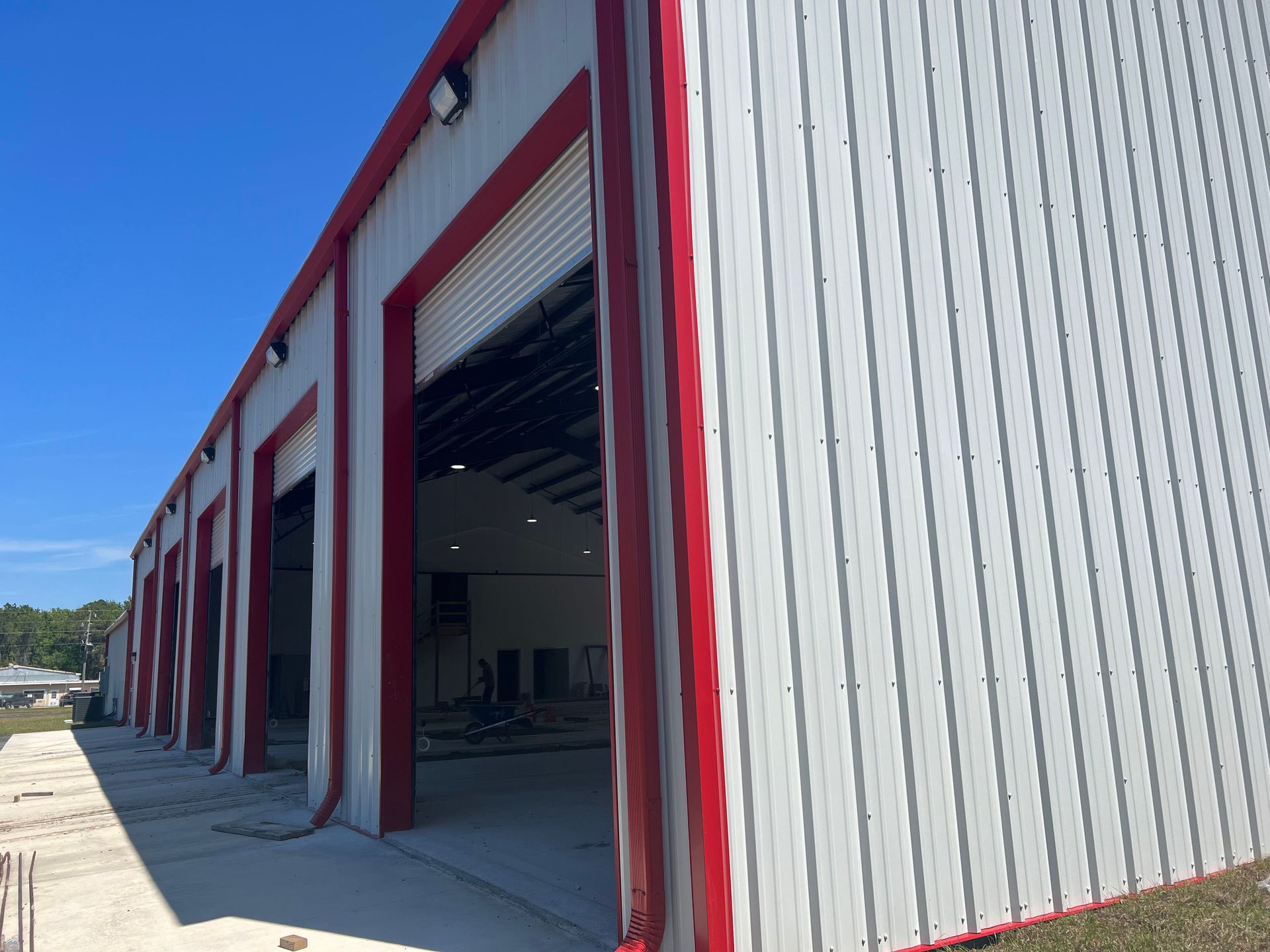 Exterior of a red-and-gray industrial warehouse with open roll-up doors under a clear blue sky