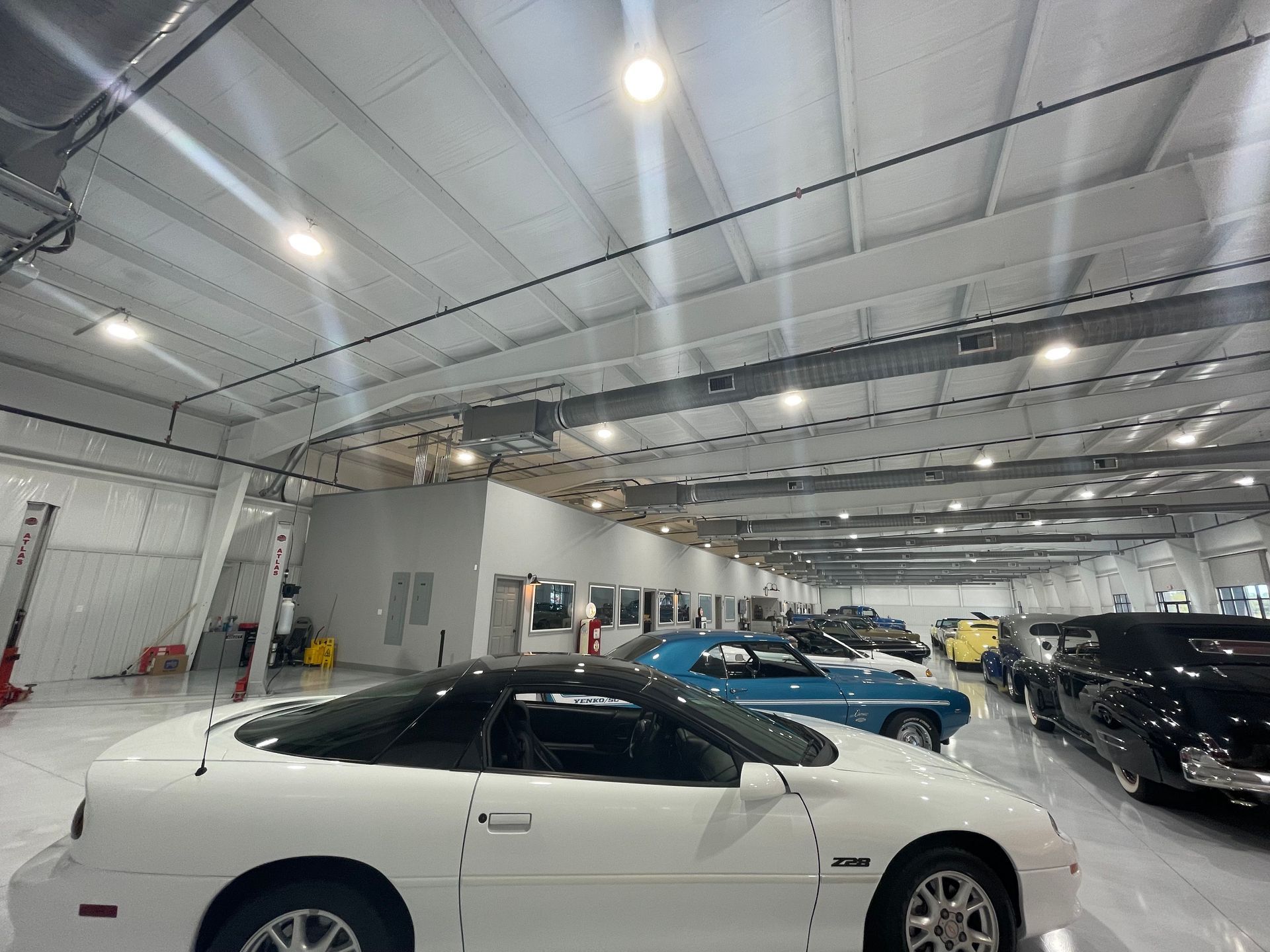 Indoor showroom with several sports cars, including a white coupe in the foreground under bright lights