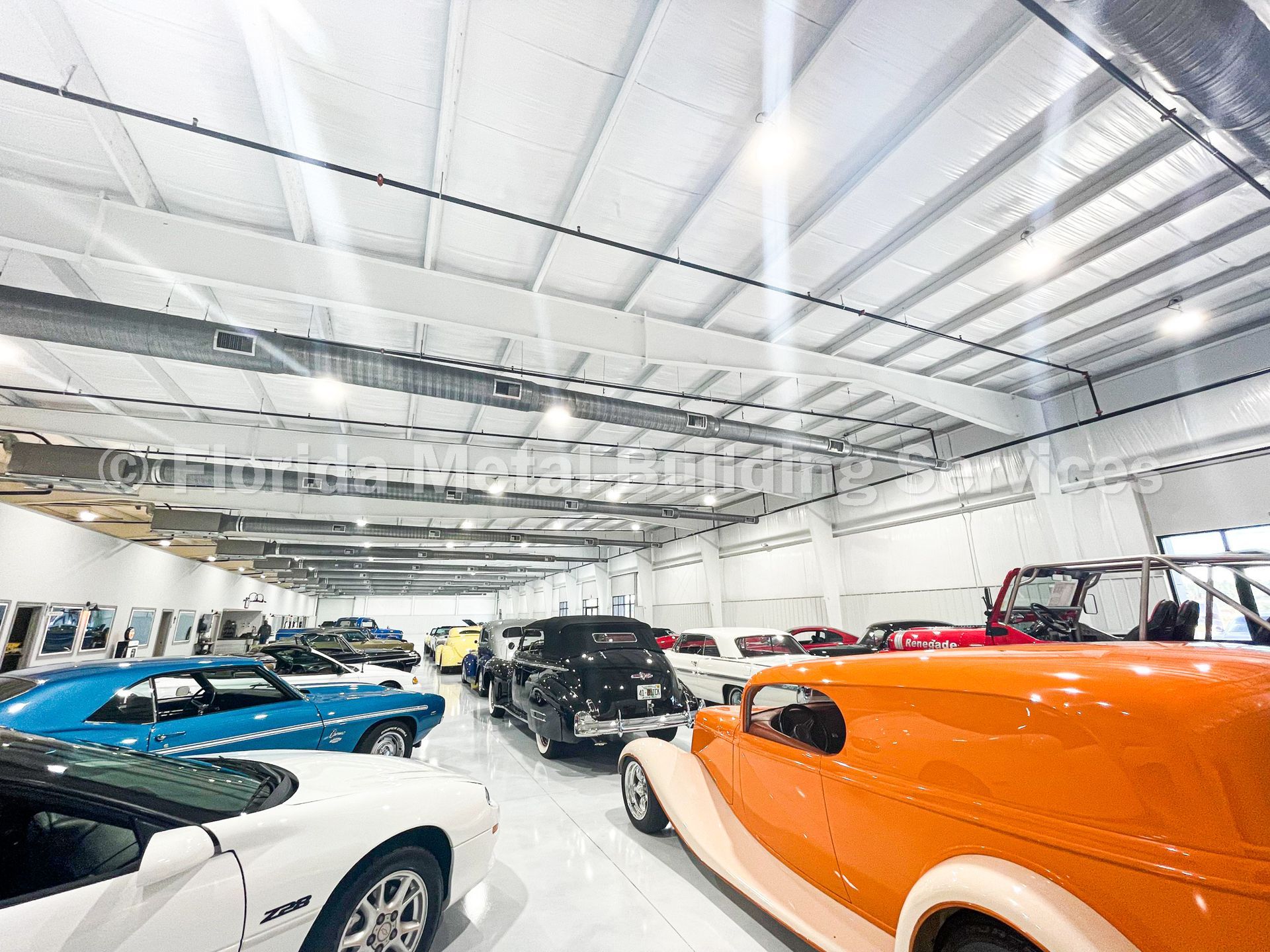 Wide view of classic cars in a bright indoor showroom, including orange, blue, white and black vehicles.