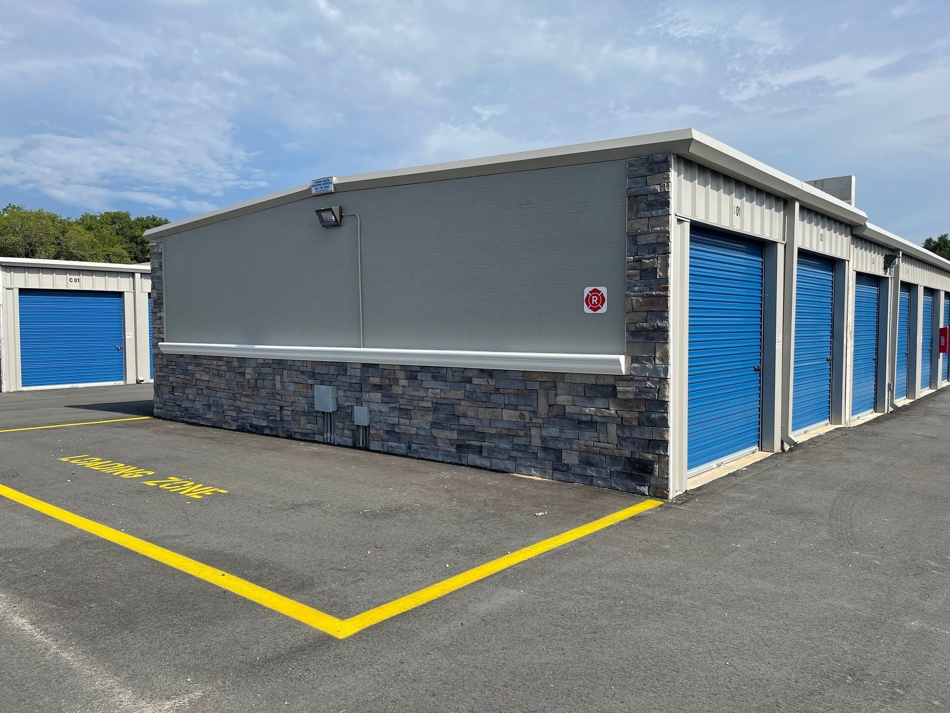 Row of blue storage unit doors on a gray building with yellow parking lines under a partly cloudy sky