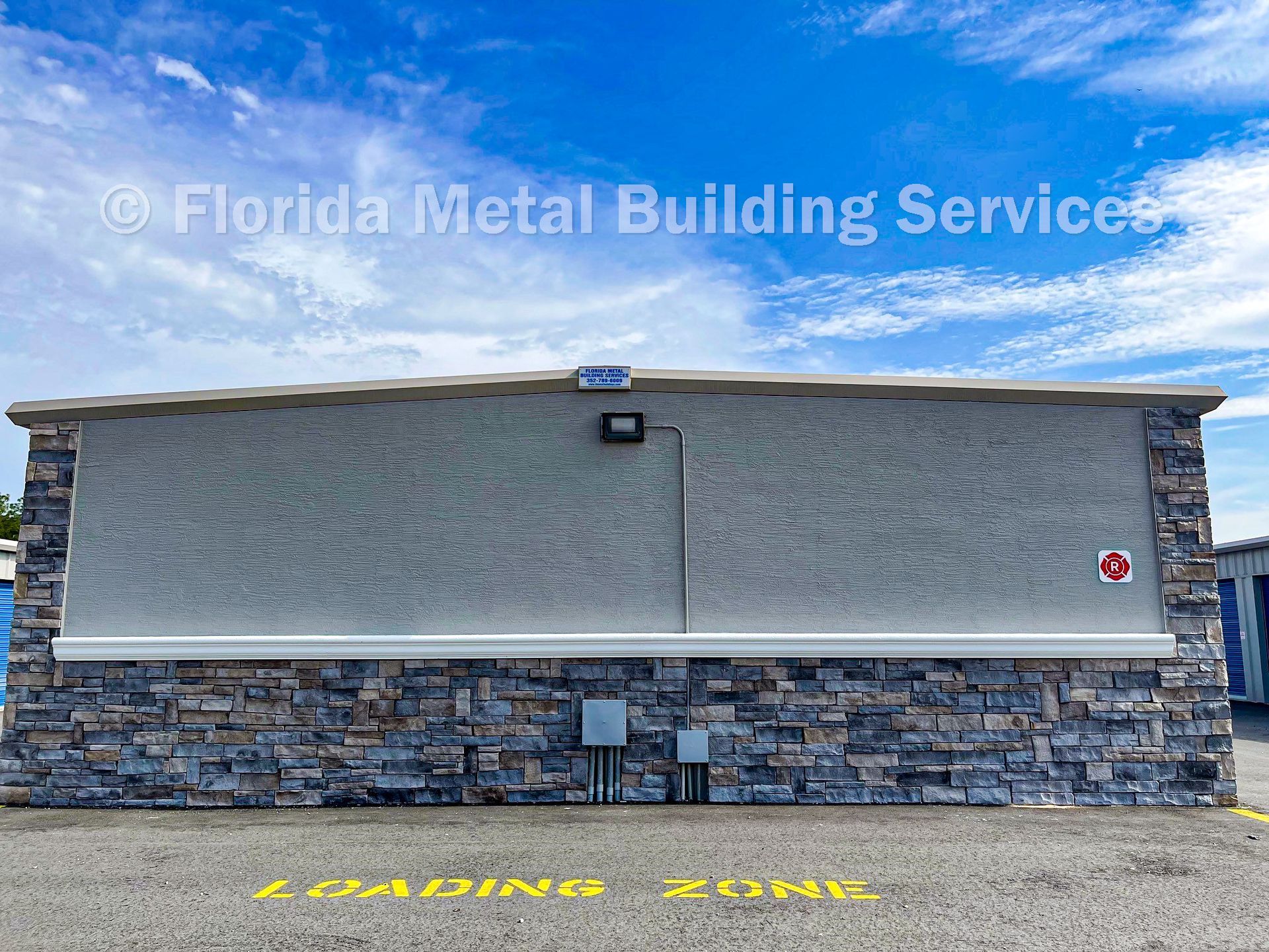 Blue-gray metal building facade with stone base under a clear sky and a yellow caution marking on the pavement