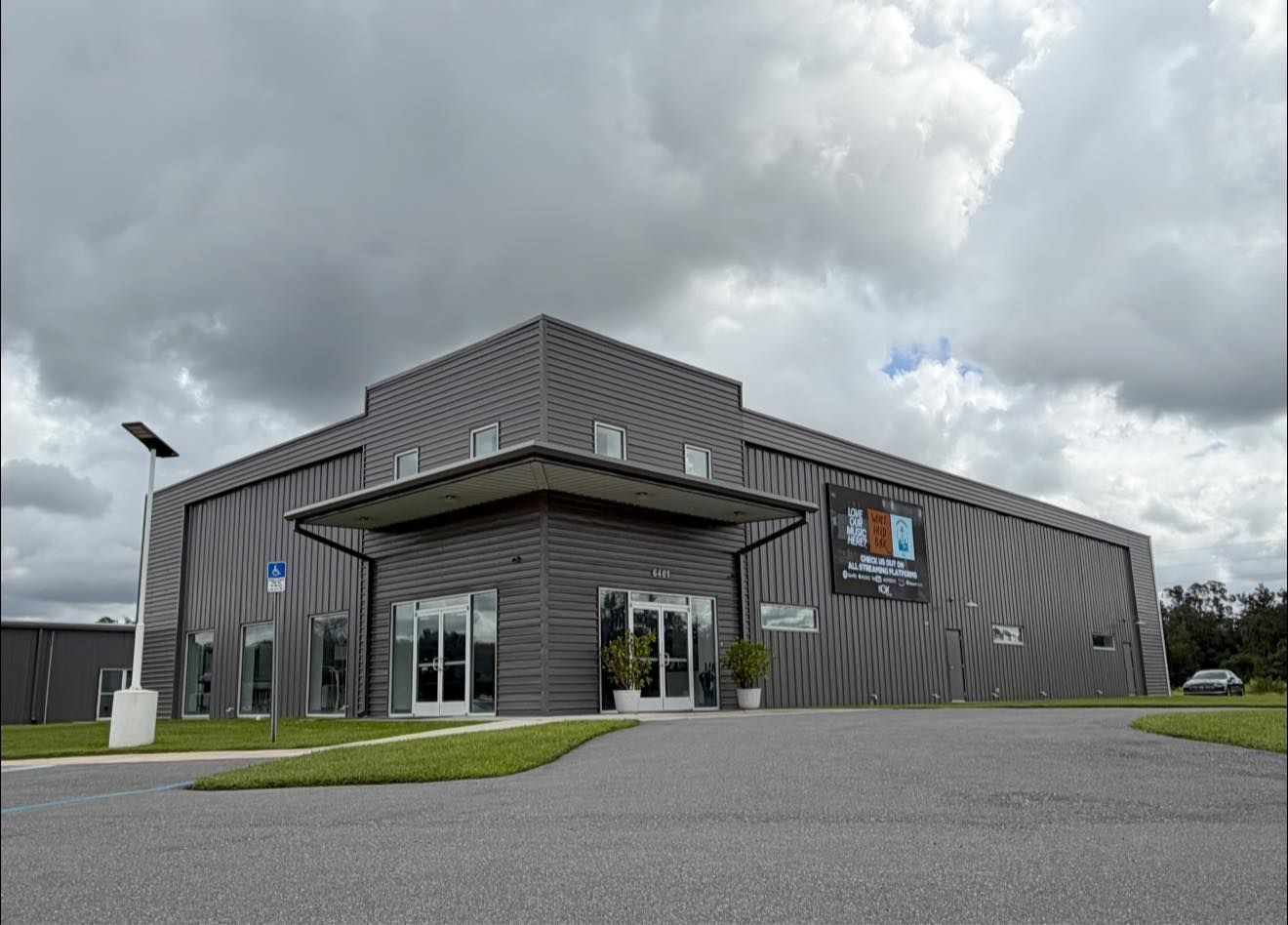 Modern gray building with a glass entrance, sign, and cloudy sky above a paved lot