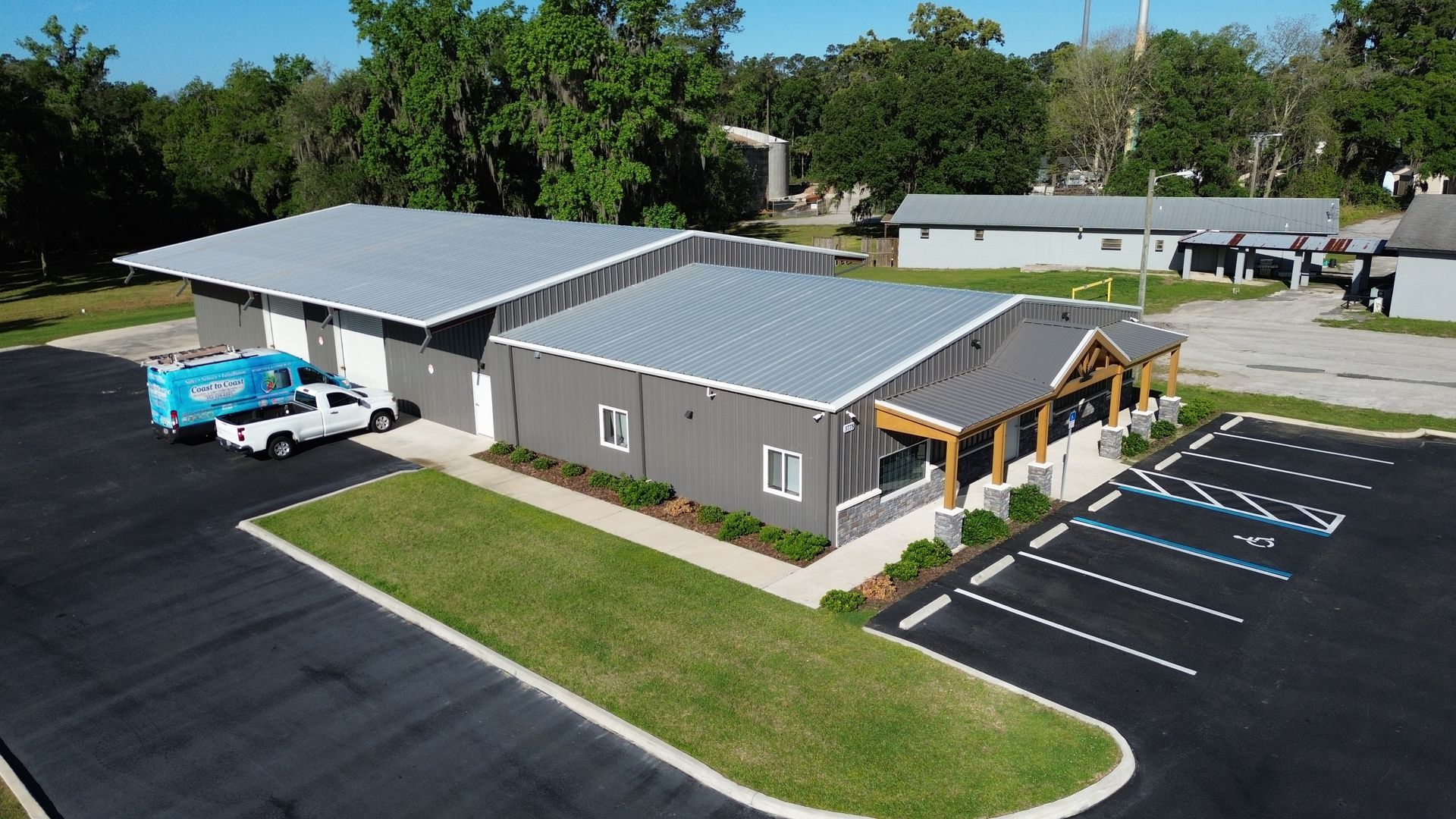 Aerial view of a gray commercial building with a metal roof, parking lot, and blue truck outside