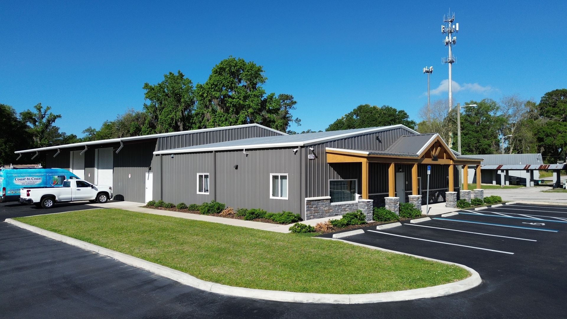 Single-story gray building with a wood entrance, parking lot, and blue sky.