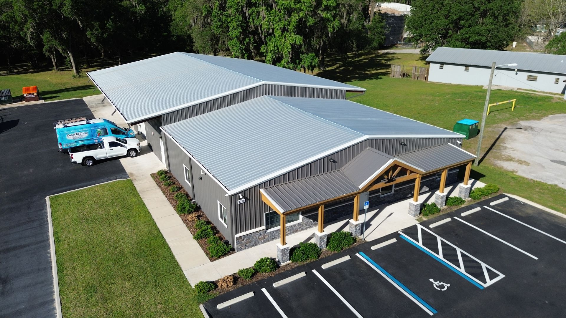 Aerial view of a gray-roofed building with parking lot, blue truck, and green lawn.