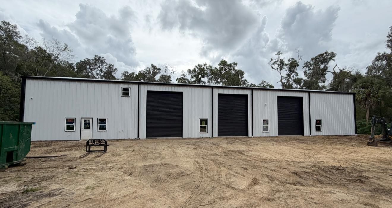 White metal warehouse with multiple roll-up doors on a dirt lot under a cloudy sky