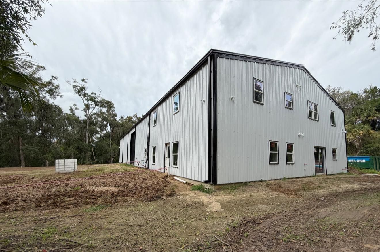 White metal industrial building with a gray roof on a dirt lot, viewed from the corner.