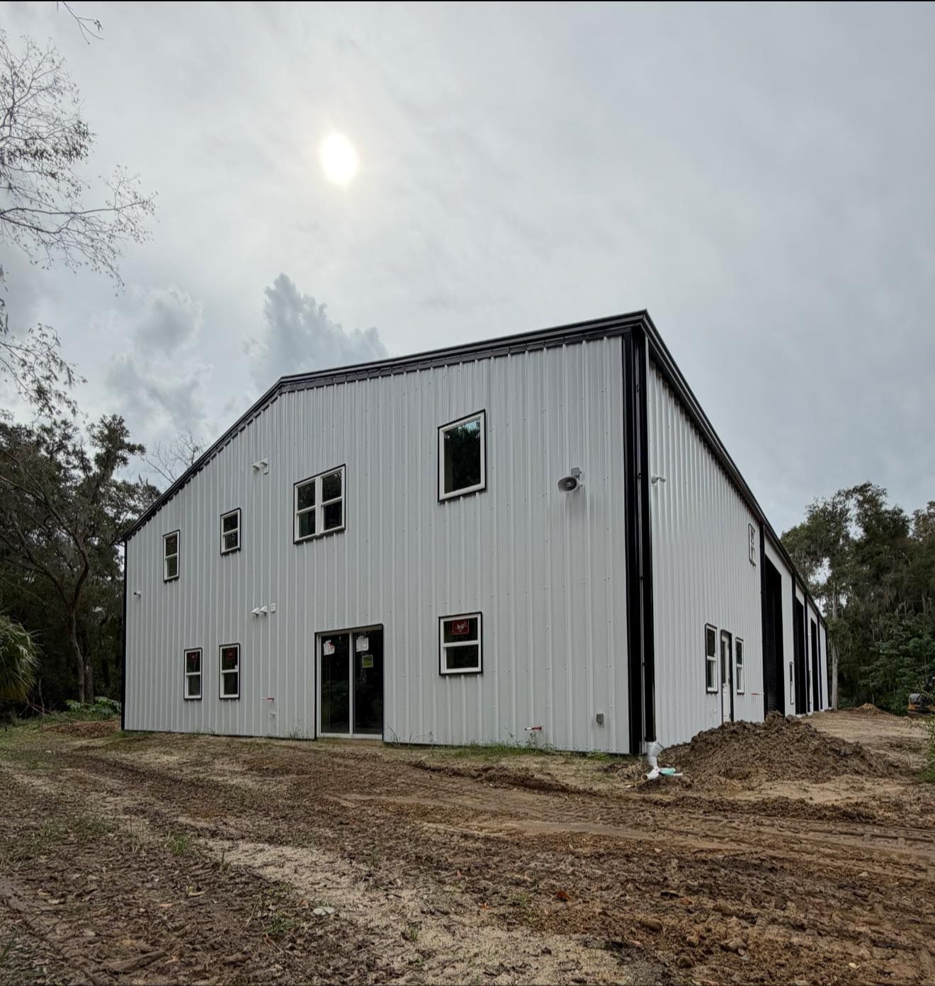 White metal building under construction on a muddy lot with overcast sky
