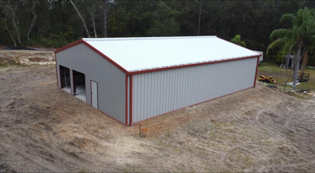 Large metal storage shed with white roof and gray walls on a cleared dirt lot.