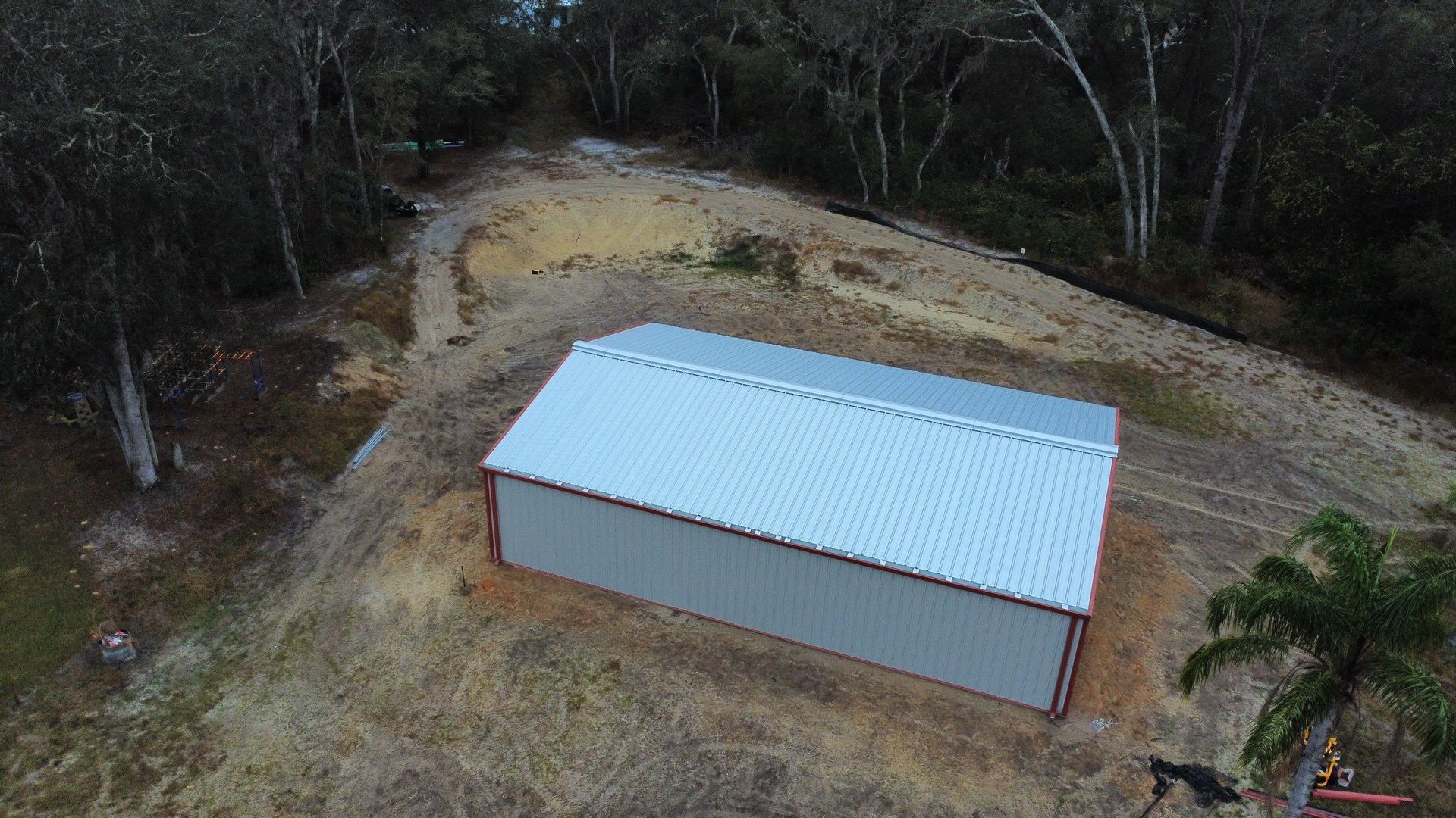 Aerial view of a small brown shed with a white roof beside a curved dirt path in a wooded area