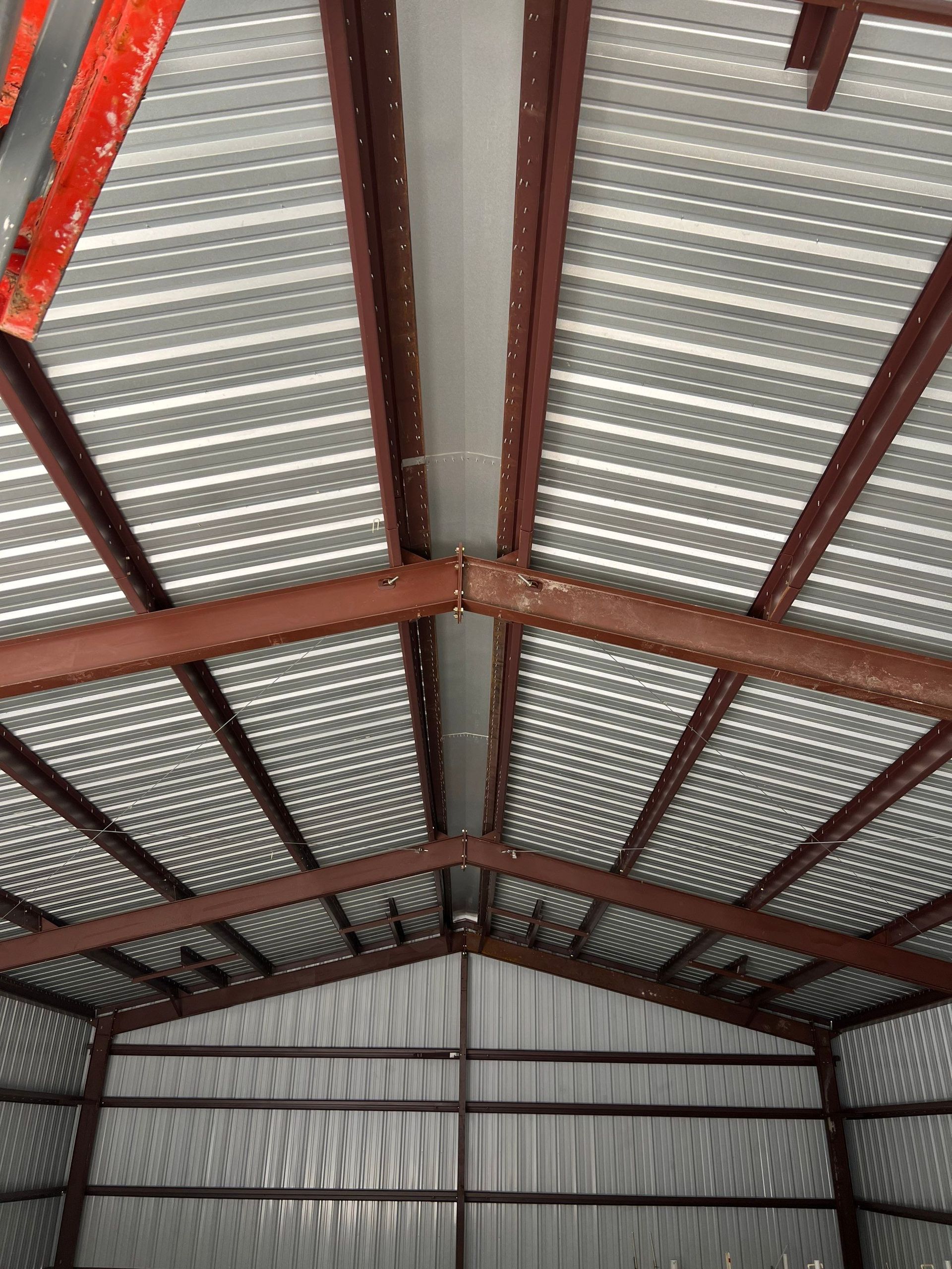 Interior of a corrugated metal roof with red steel beams in a warehouse or shed