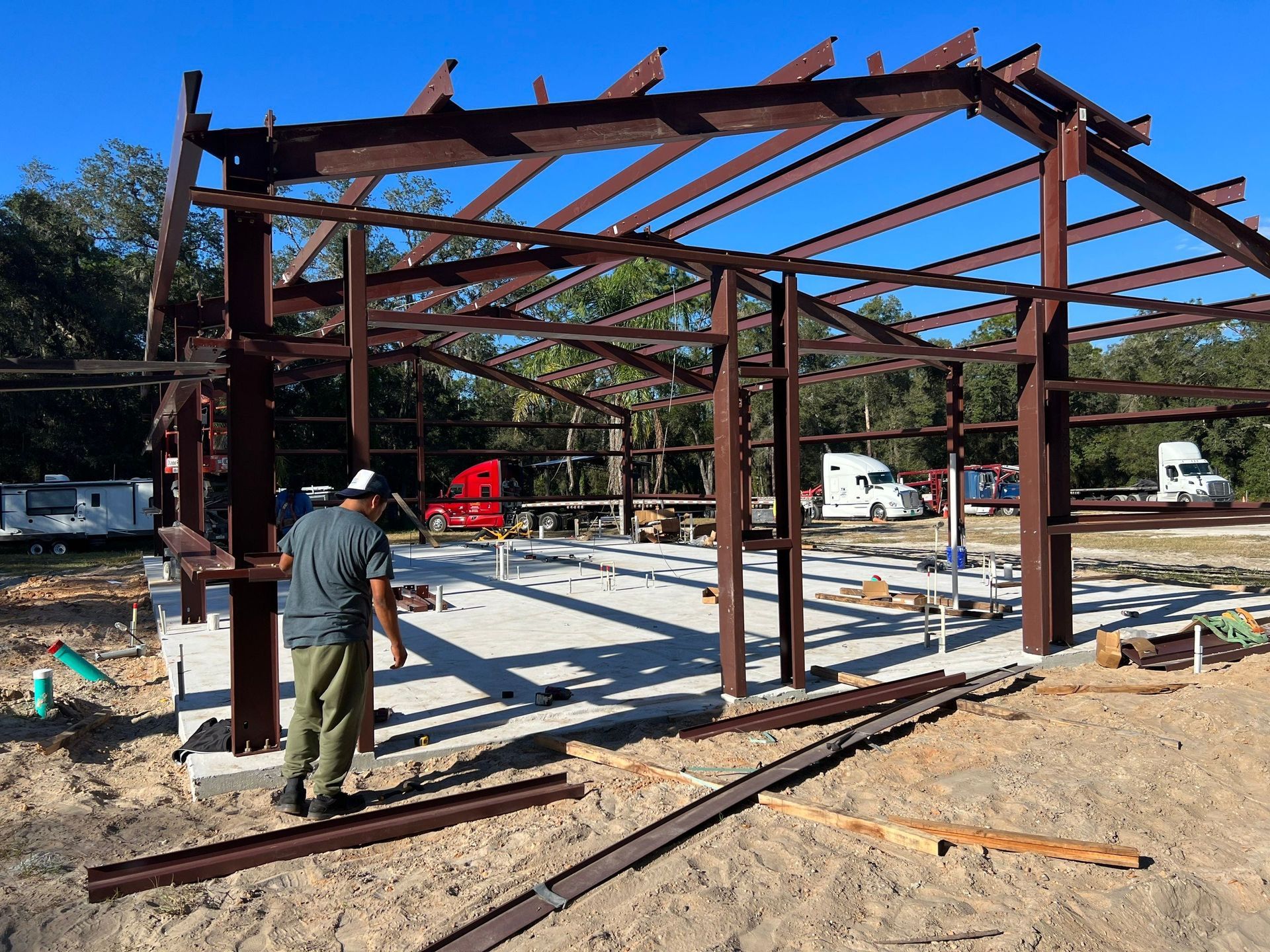 Steel frame under construction with a worker on site and construction materials scattered around