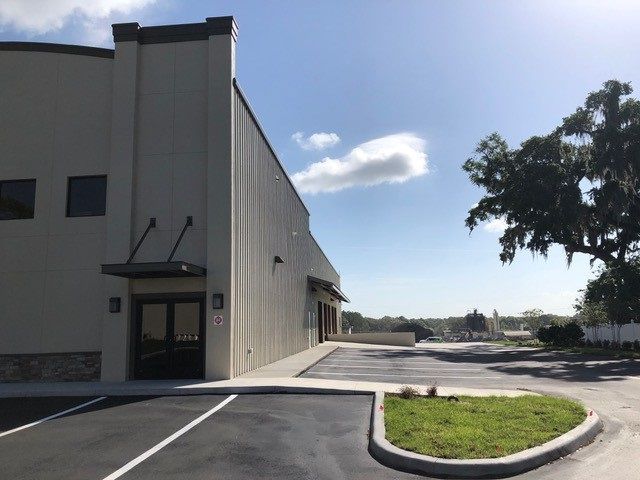 Industrial building entrance with empty parking lot, sidewalk, and trees under a sunny sky