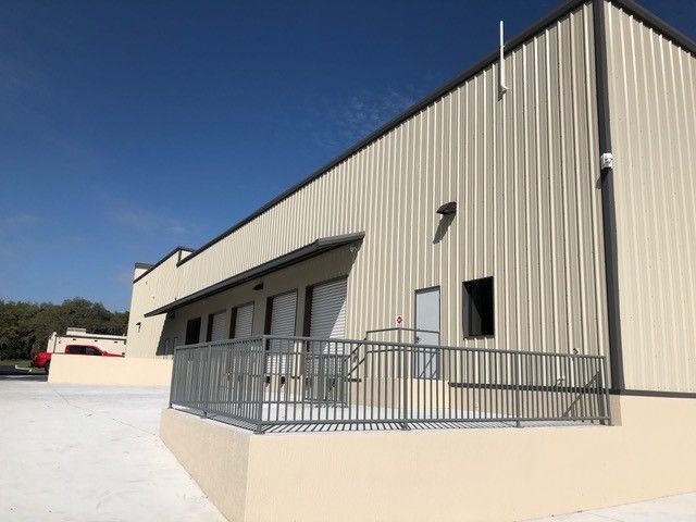 Side of a beige industrial building with loading docks and metal railings under a blue sky