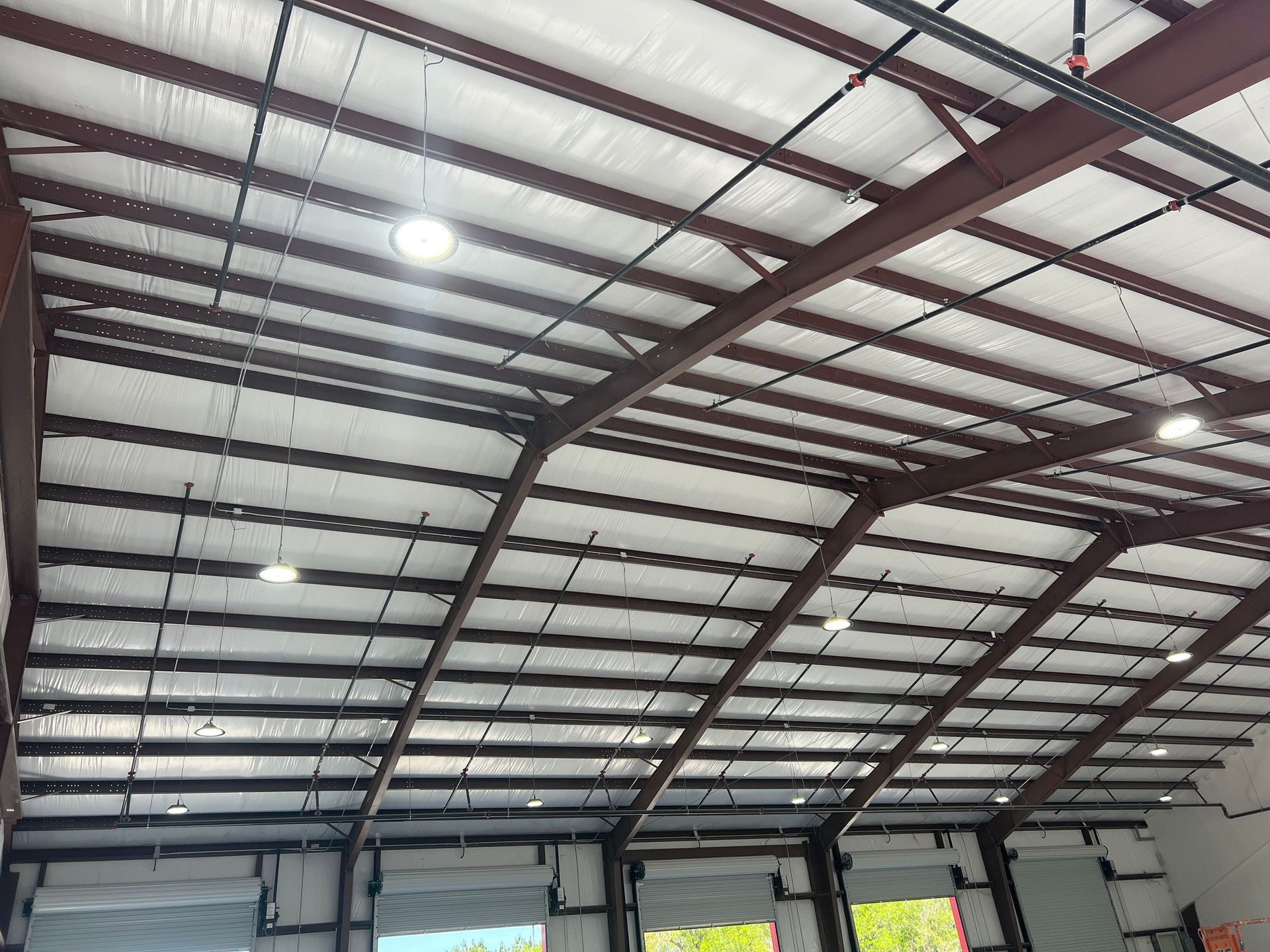 The interior of a high-ceiling industrial warehouse with metal beams, reflective insulation panels, and pendant lights.