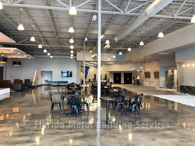 Large industrial hall with rows of chairs and tables under high ceilings and bright hanging lights