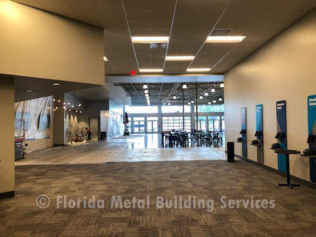 Empty modern lobby with tiled floor, ceiling lights, glass entrance, and kiosk stations along the wall