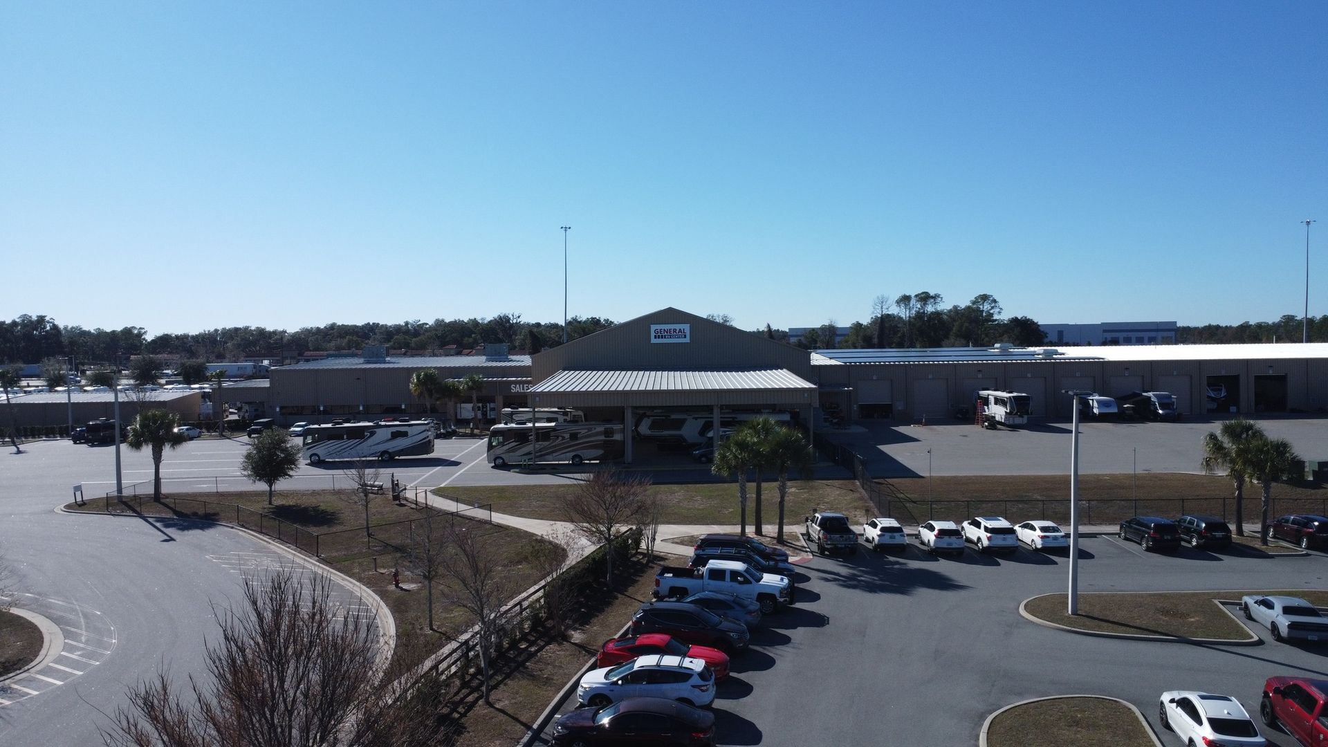 A multi-building complex with a large parking lot full of cars and several recreational vehicles under a covered area.
