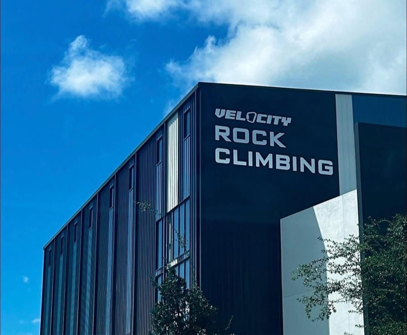 The exterior of a Velocity Rock Climbing building with dark panels and white lettering against a bright blue sky.