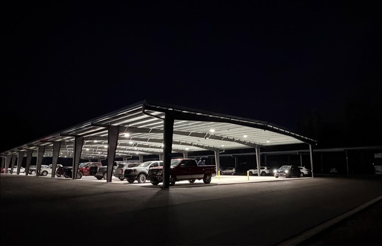 A covered parking structure illuminated by overhead lights at night, with several parked vehicles visible underneath.