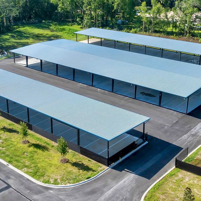 An aerial view of three rows of empty, blue-roofed parking carports surrounded by paved areas and grassy patches.