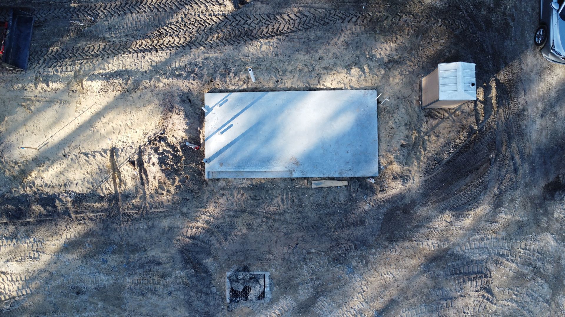 An aerial view of a rectangular concrete foundation slab set in a dirt construction site with a nearby portable toilet.