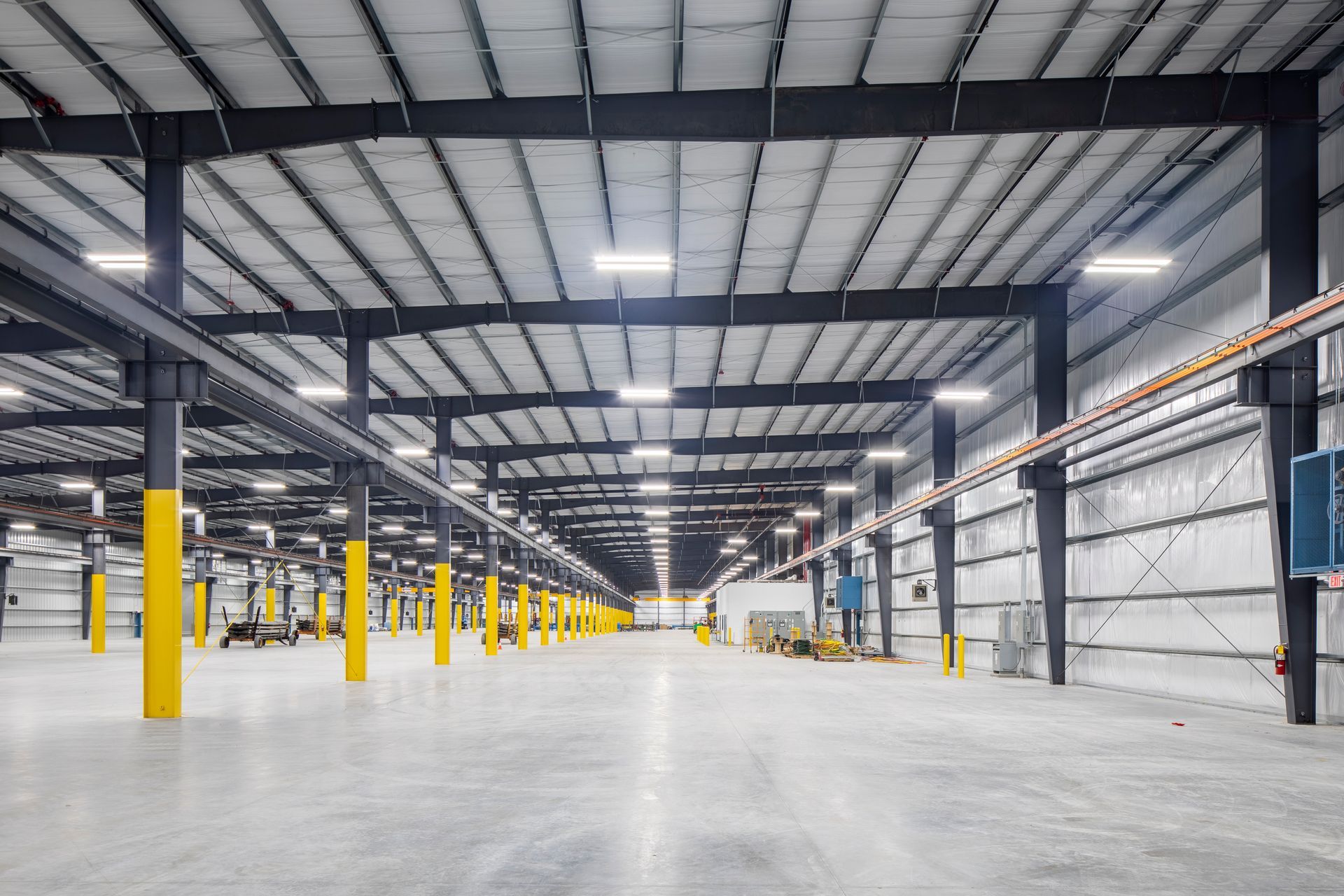 A vast, empty industrial warehouse with high ceilings, concrete floors, and rows of yellow support columns.