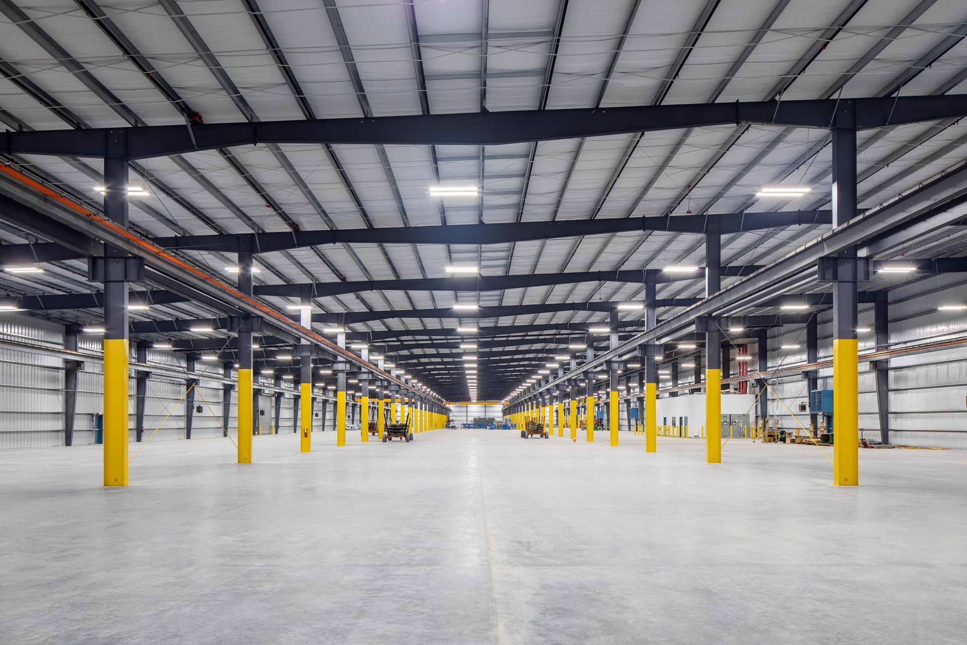 A wide, empty industrial warehouse with a high ceiling, concrete floor, and rows of yellow-painted support pillars.