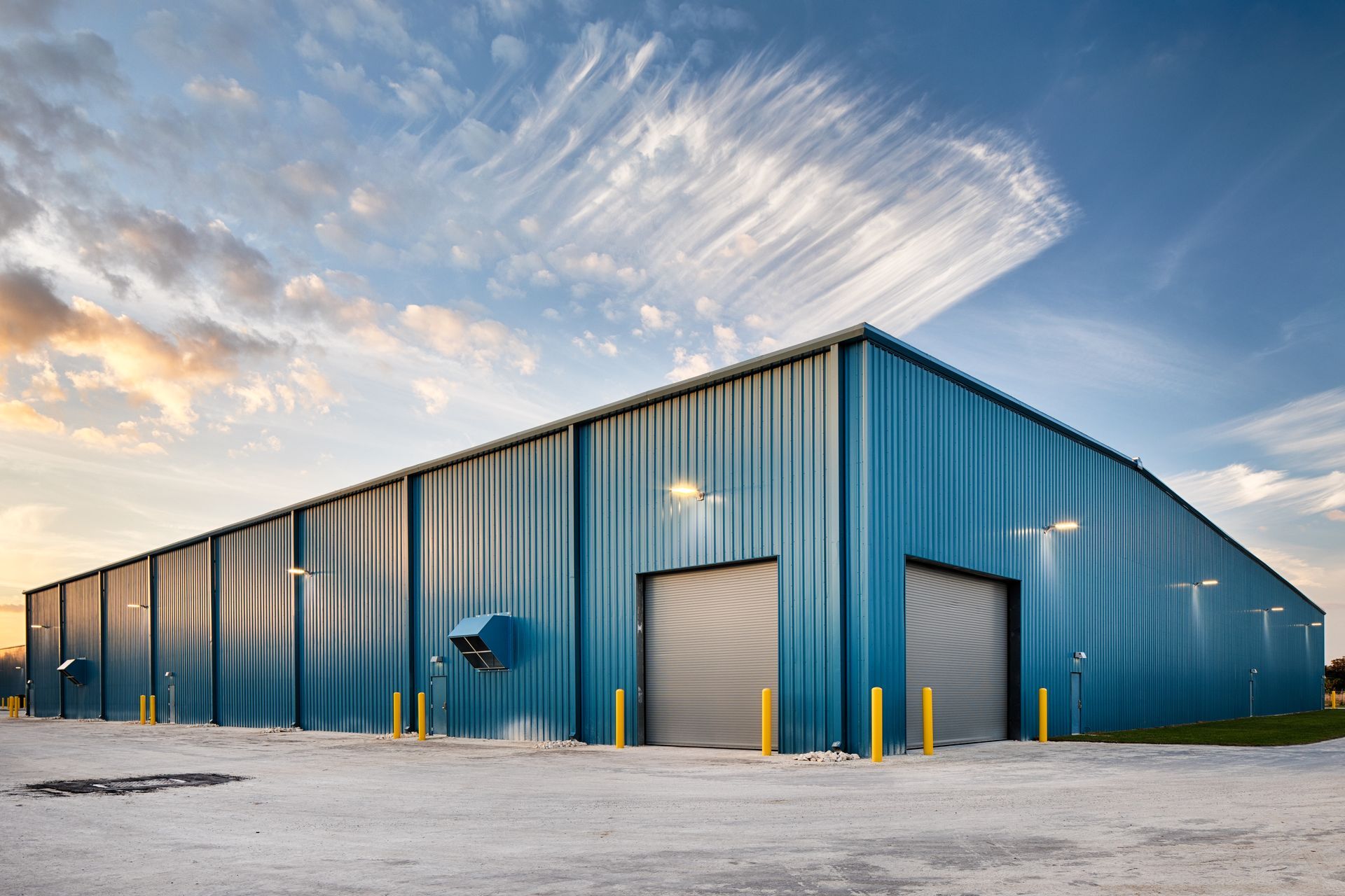 A large blue, metal-sided warehouse building with two roll-up doors under a partly cloudy sky.