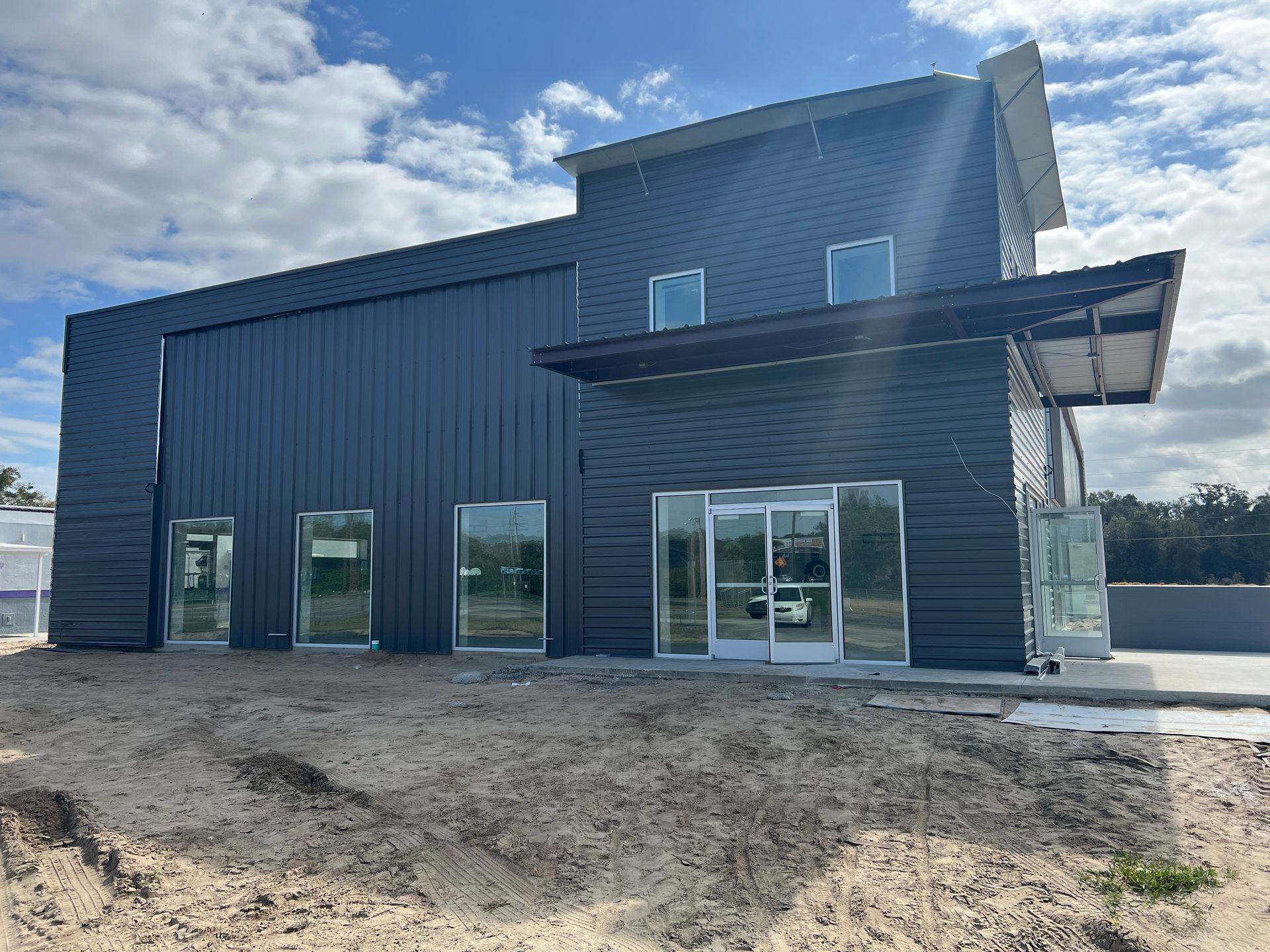 A modern, dark-sided commercial building under construction with glass entryways and a partially finished sandy lot.