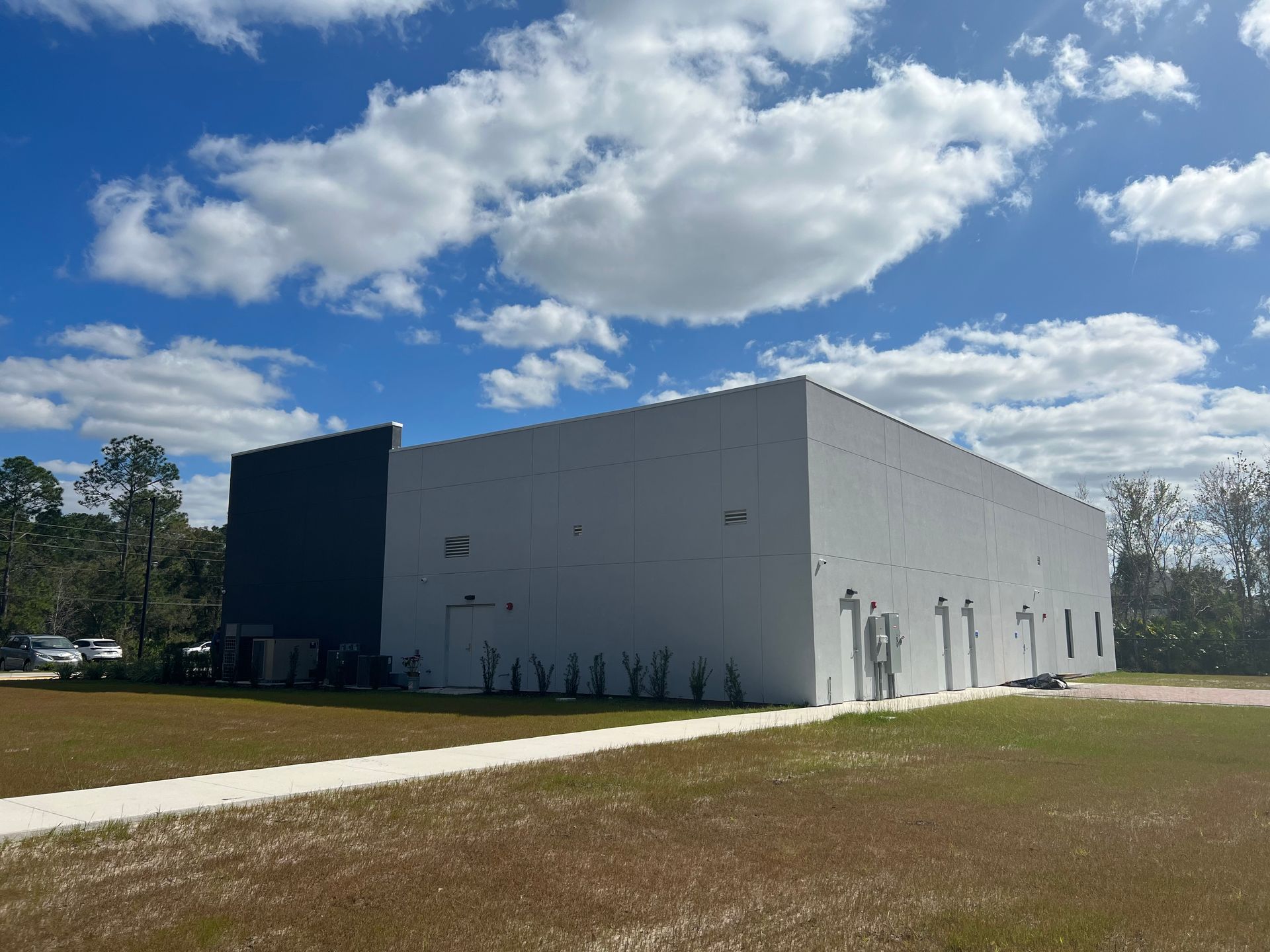 A large, rectangular warehouse building with white and dark blue exterior walls, set against a bright, cloudy blue sky.