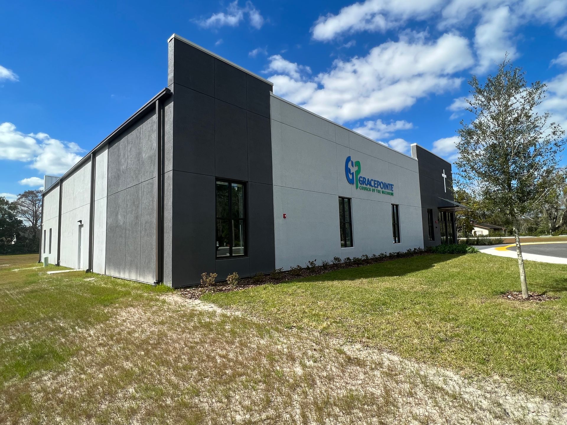 Modern building exterior with gray and white painted concrete walls, dark-framed windows, and a blue sign under a blue sky.