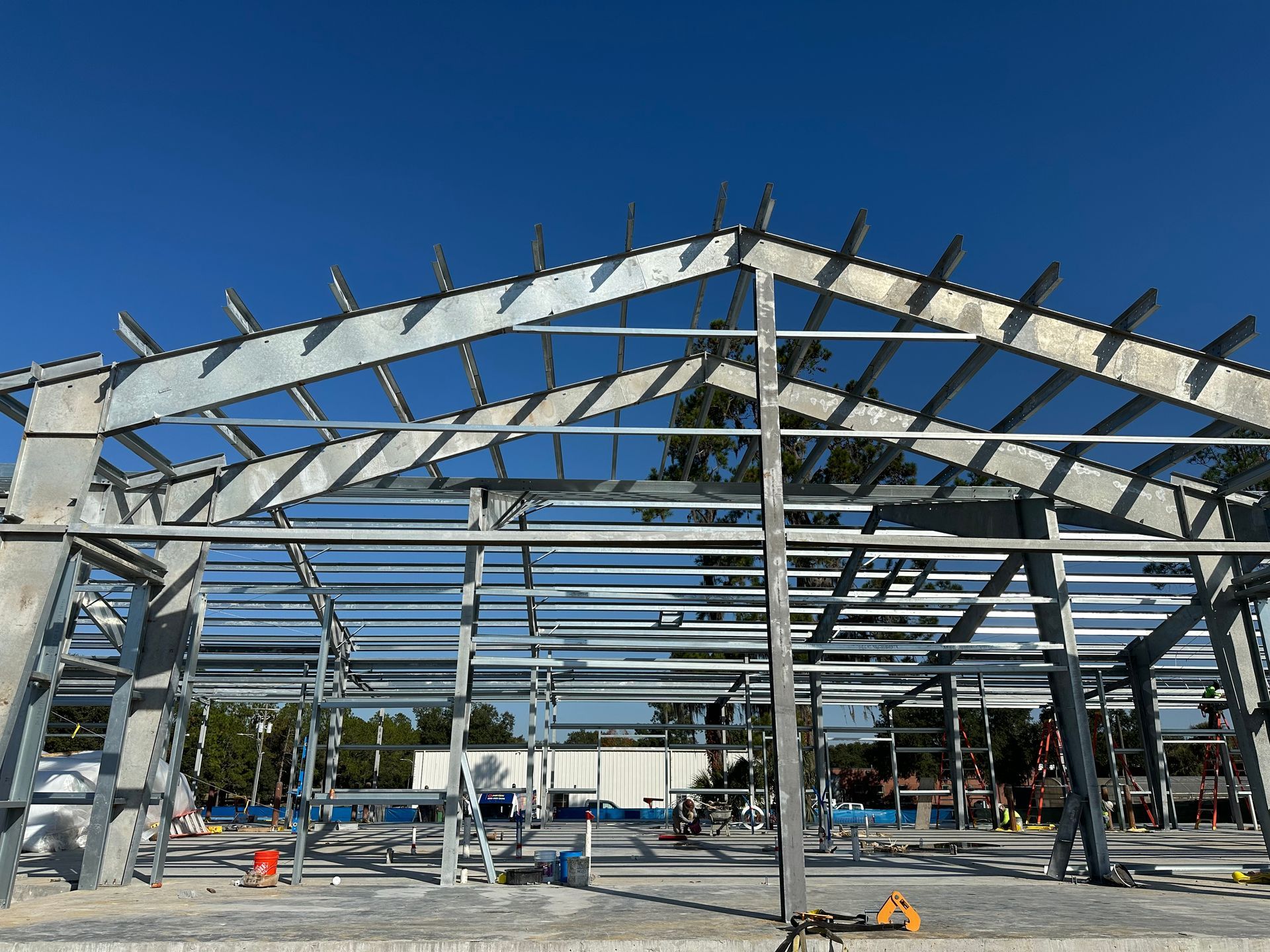 A metal frame construction site of a gabled building under a clear blue sky.