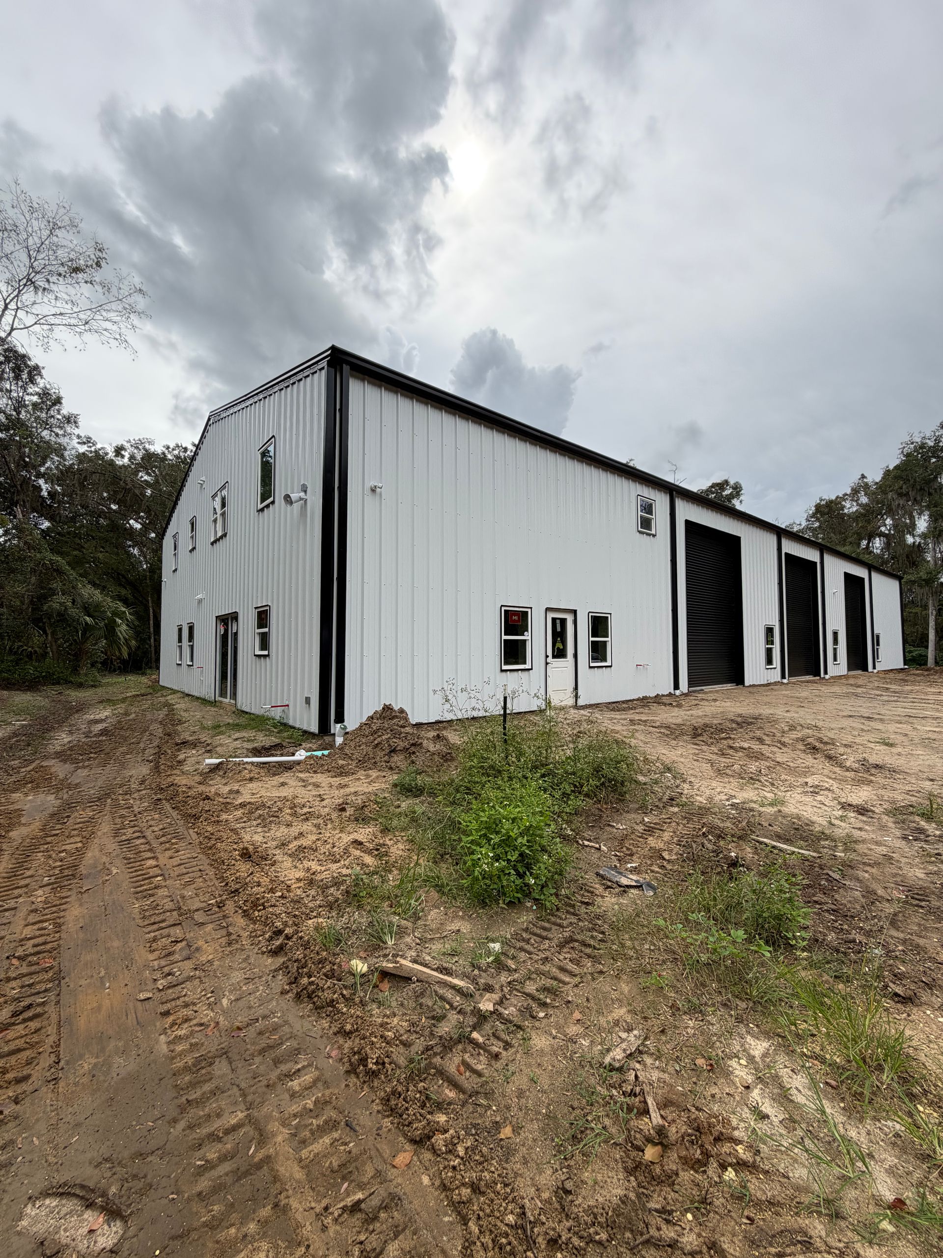 A newly constructed white metal warehouse building with black trim and roll-up garage doors on a dirt lot.