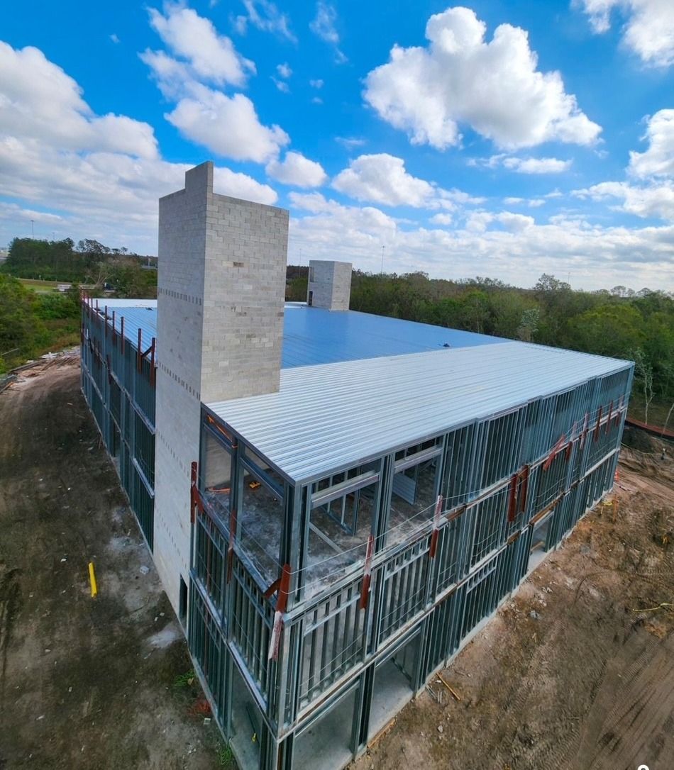 A multi-story building under construction with a metal frame and flat blue roof against a clear blue sky.