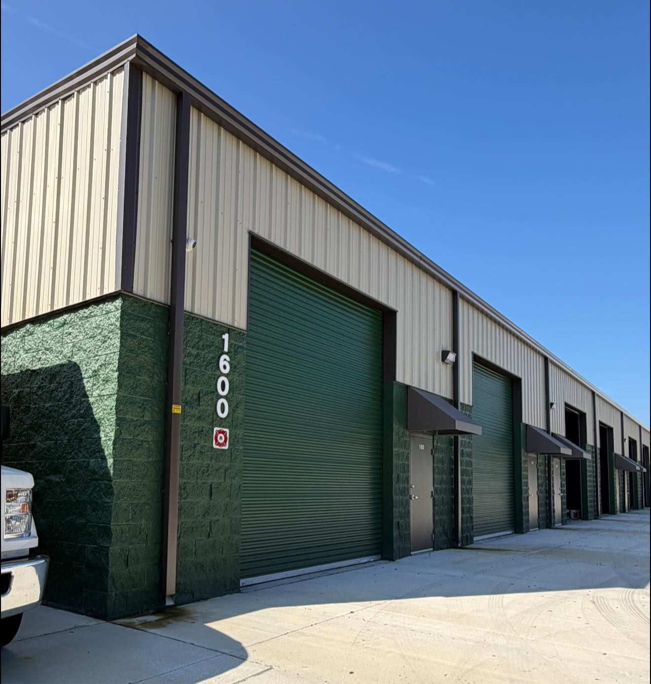 Industrial warehouse units with green roll-up doors and beige siding under a blue sky