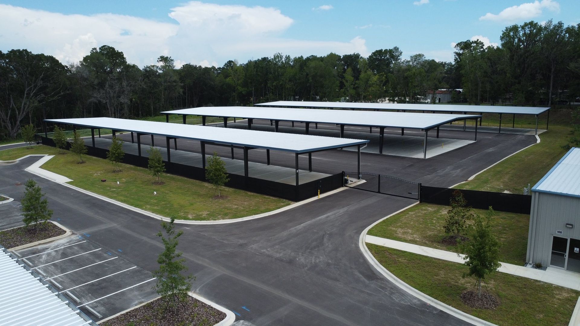 An aerial view of a parking lot with rows of white covered carports, surrounded by trees and a paved driveway.
