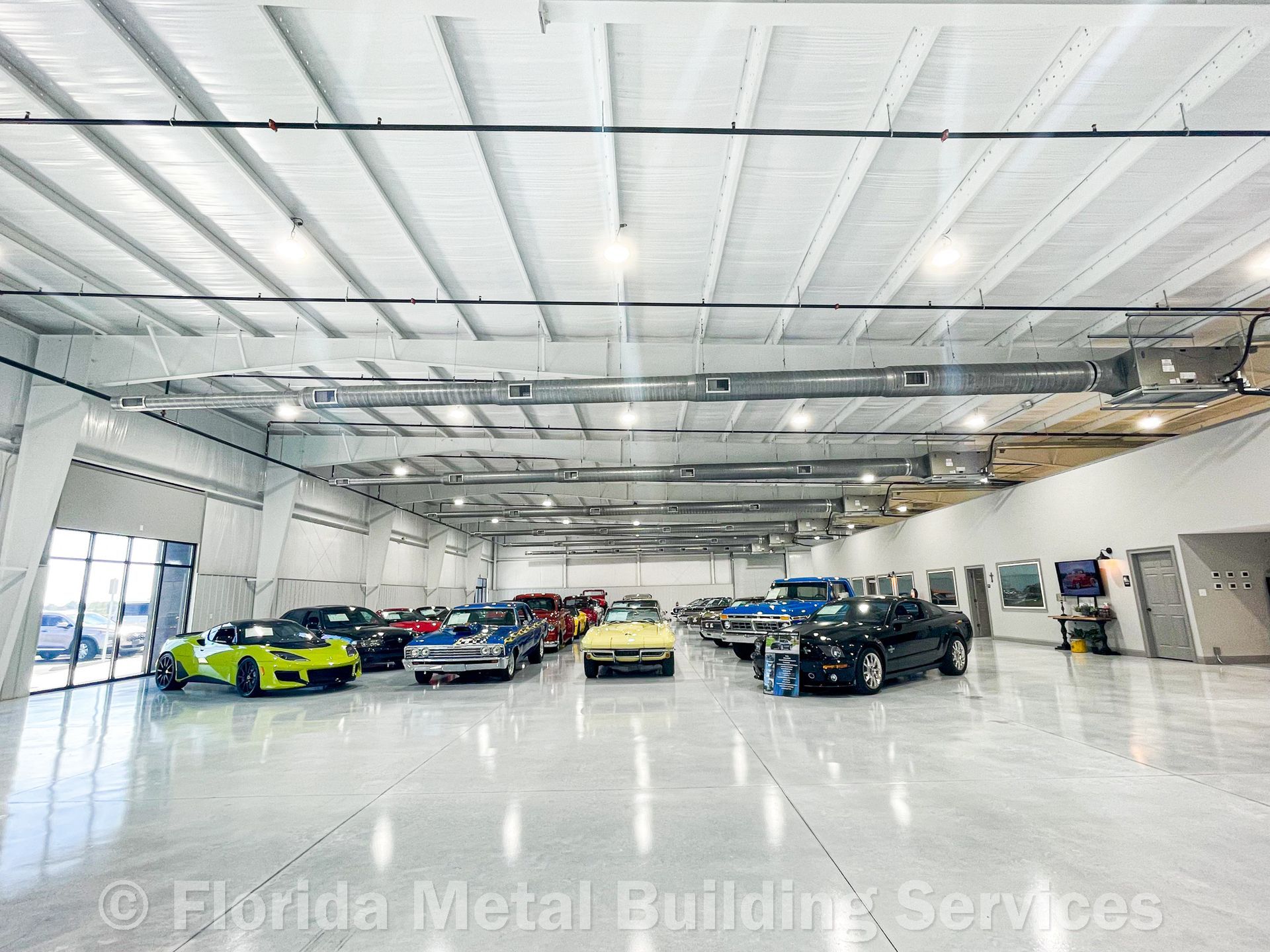 A bright, spacious indoor car showroom with polished floors and a high white ceiling, housing several collector cars.