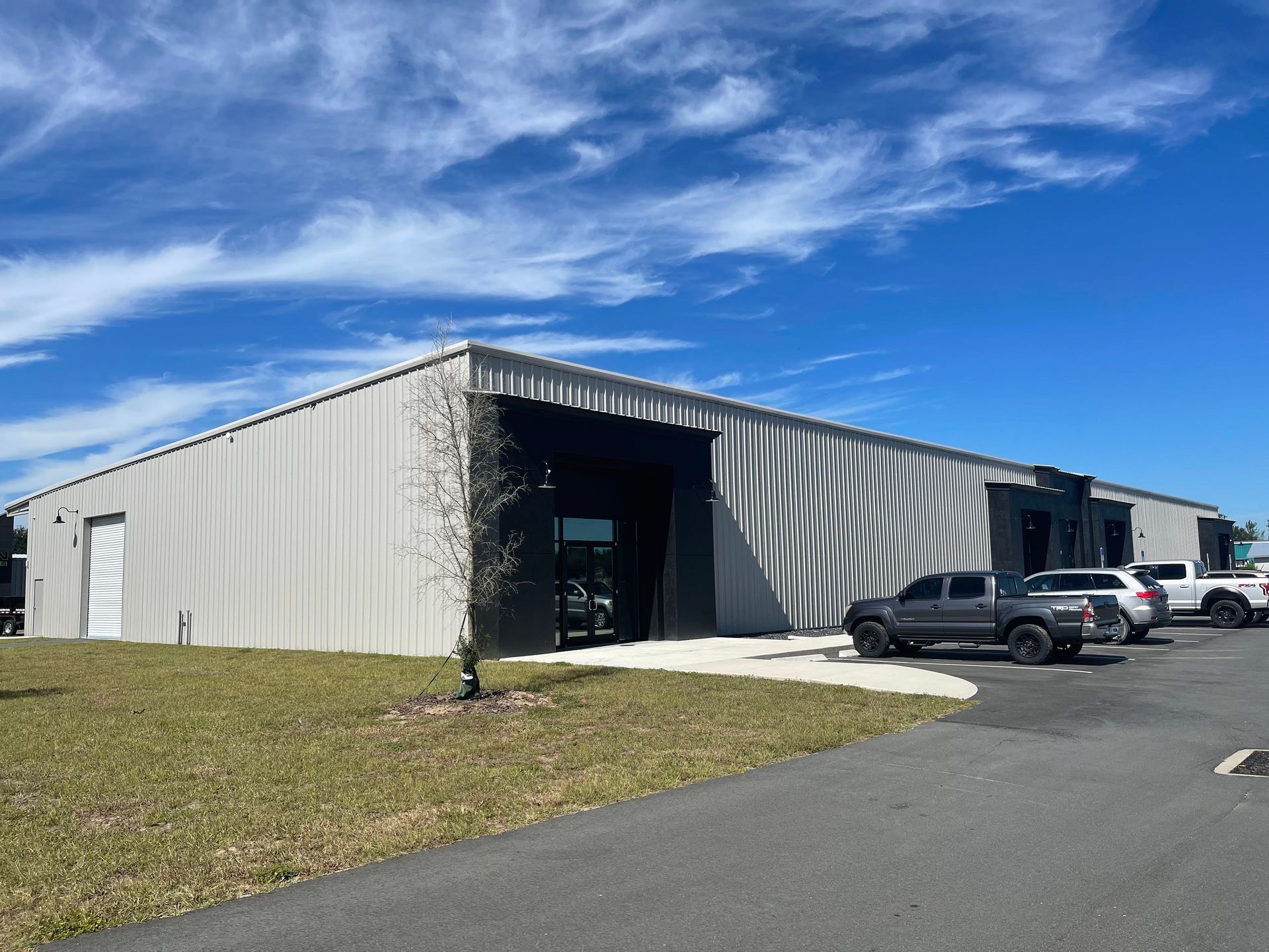 A long, light-colored industrial warehouse building with a dark entryway under a bright blue sky with scattered clouds.