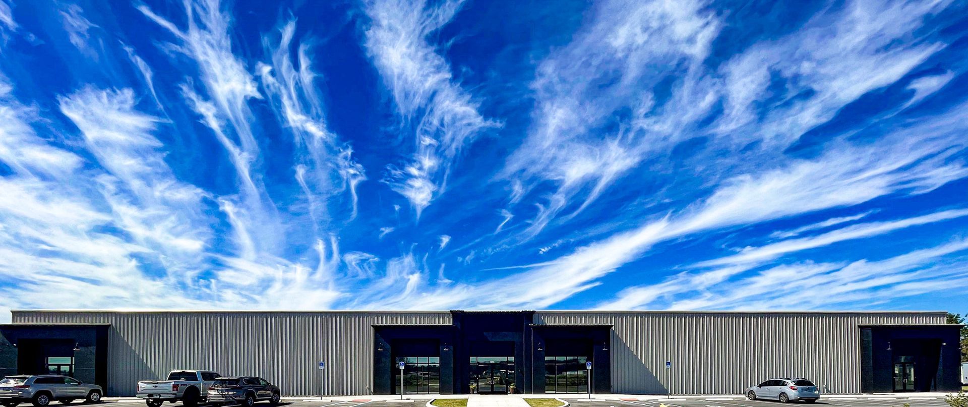 A single-story commercial building with dark entrances sits under a vibrant blue sky filled with sweeping cirrus clouds.