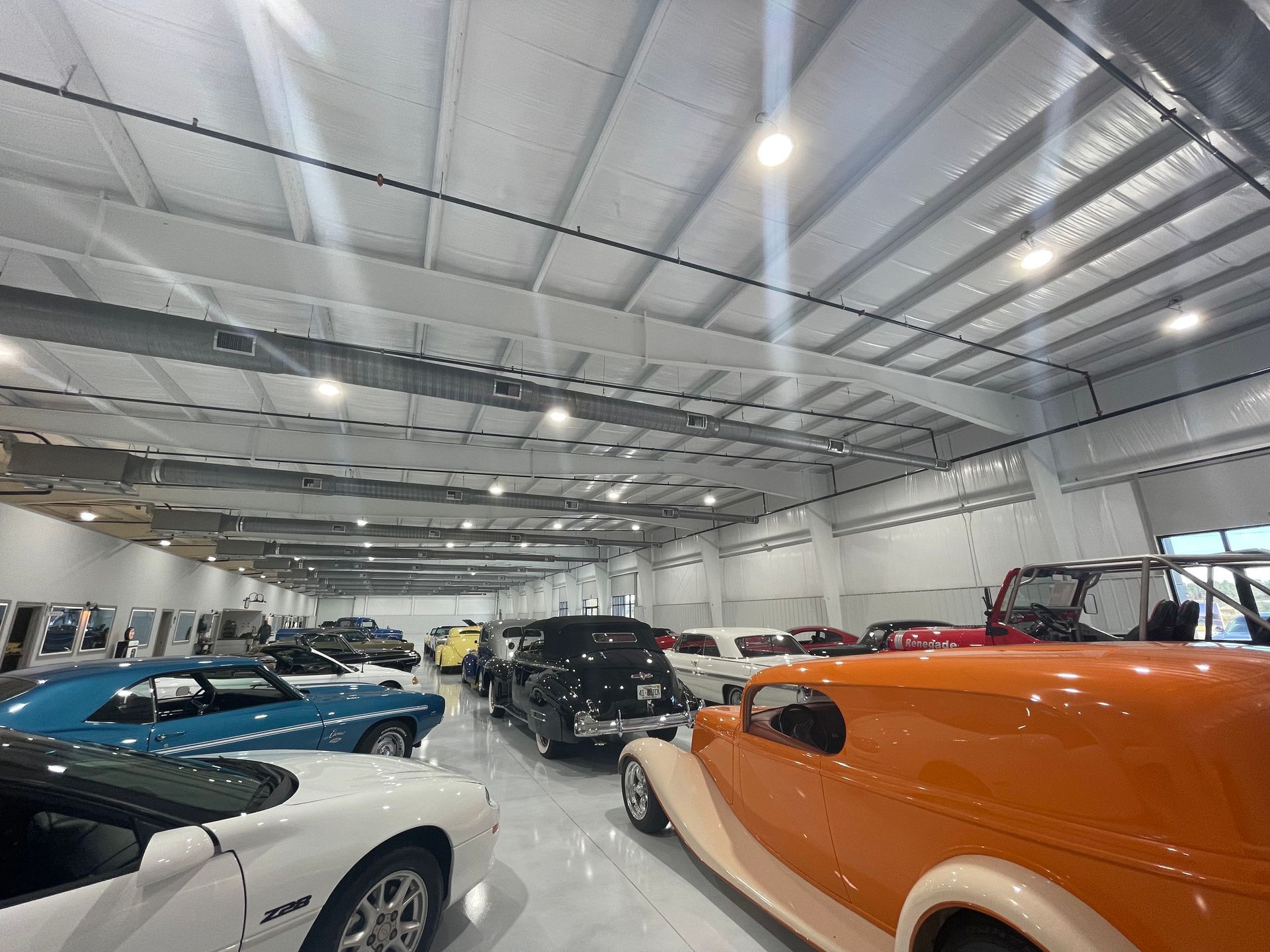A spacious garage filled with various classic and modern collector cars, including bright orange and blue models.
