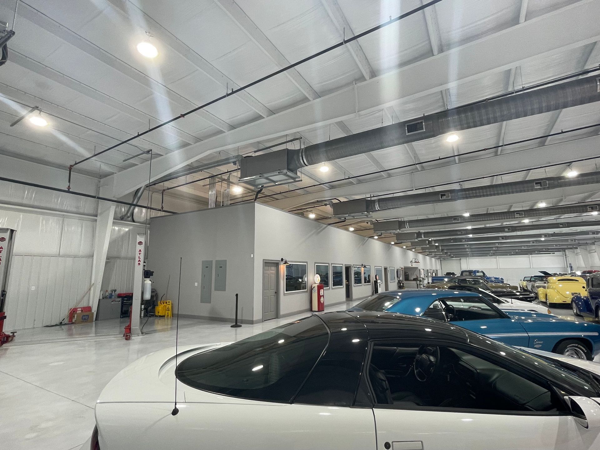 A bright, spacious indoor garage featuring several parked cars, including a white vehicle in the foreground.